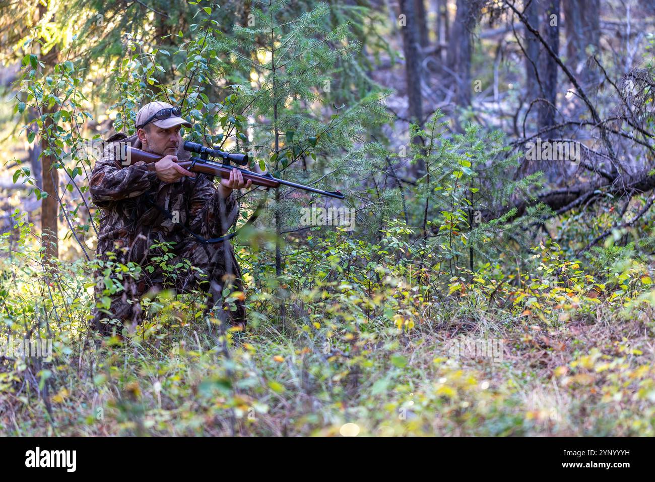 Hunter con abiti mimetici in posizione di semiinginocchiamento, tenendo in mano un fucile mentre si avvicina lentamente al gioco, pronto a sparare in qualsiasi momento. Caccia. Foto Stock