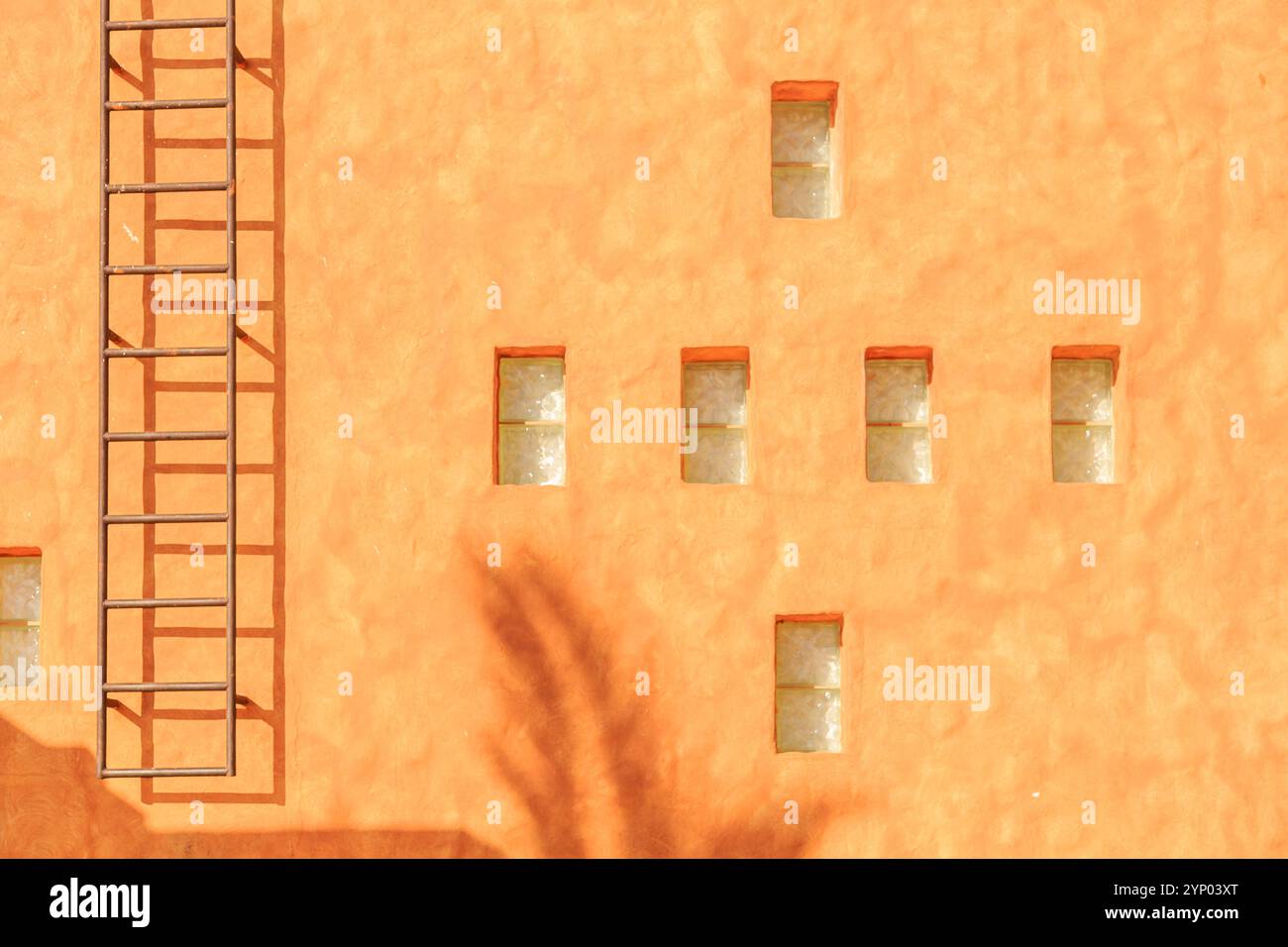 Un edificio con una scala laterale e una fila di finestre. L'edificio e' arancione e presenta un design unico con una croce sul muro Foto Stock