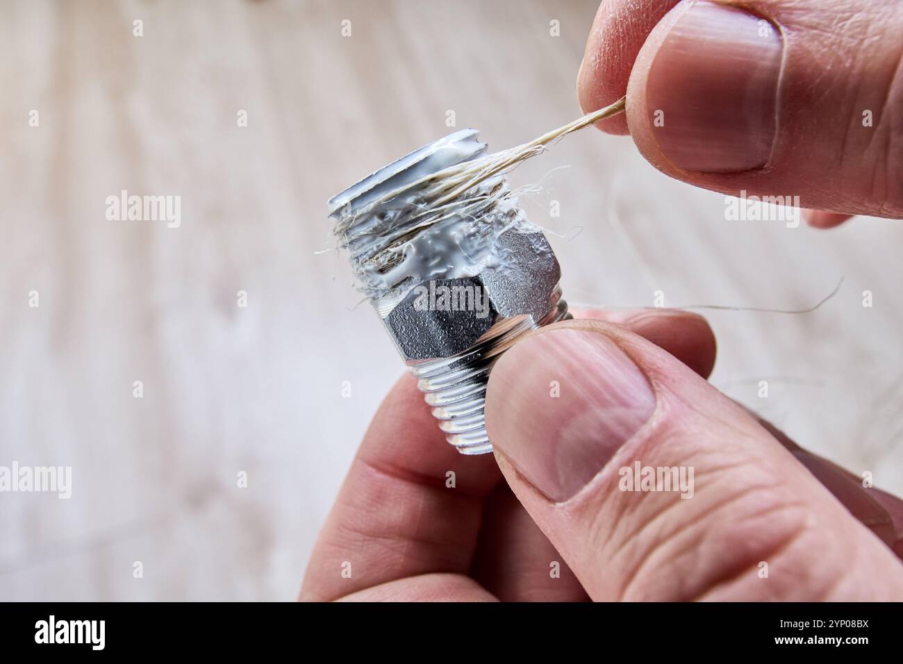 Avvolgere la canapa sulla filettatura del raccordo del tubo sopra il sigillante per sigillare le perdite. Foto Stock