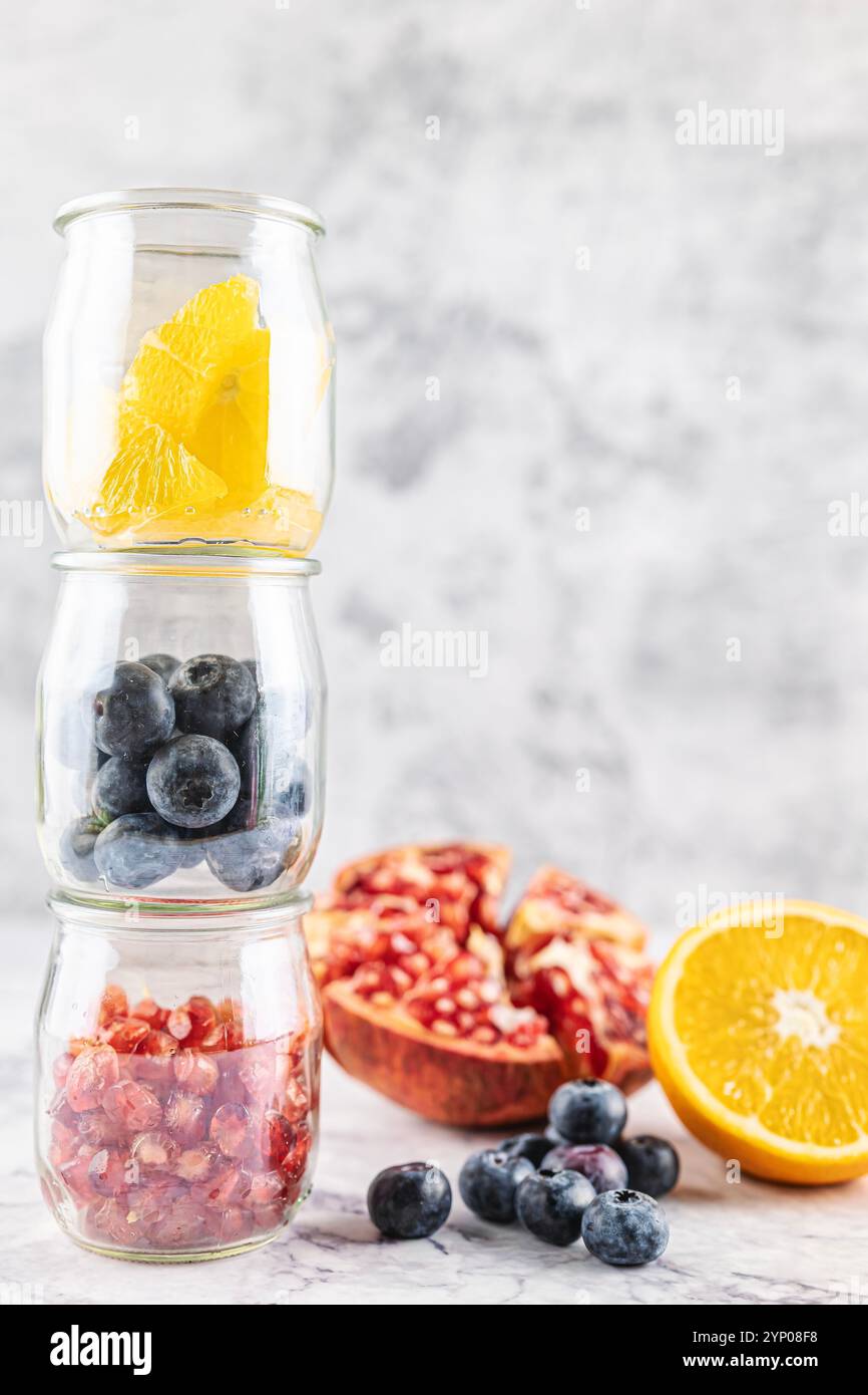 Frutta antiossidante e antinfiammatoria, melograno, arancia e mirtilli in vasetti di vetro che formano una torre. Concetto di prevenzione delle malattie e di salute Foto Stock