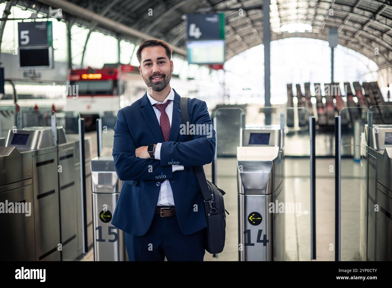 un uomo d'affari del copyspace con una tuta si posa con le braccia incrociate alla stazione ferroviaria, in attesa di dirigersi verso il suo posto di lavoro, trasudando fiducia e prontezza Foto Stock