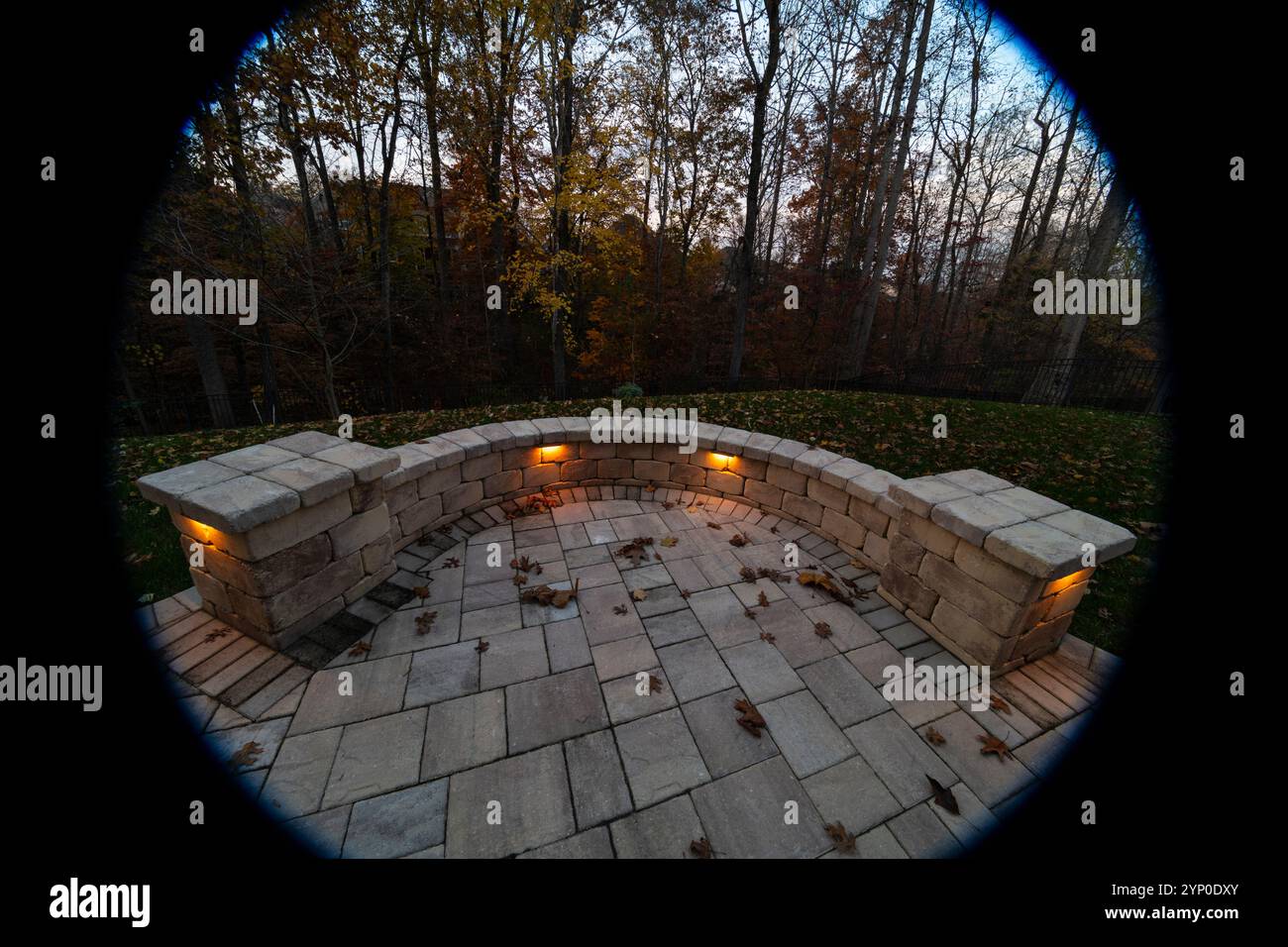 Un patio in pietra curvo con luci calde incorporate che si illuminano sullo sfondo di una foresta autunnale buia, creando un'atmosfera intima e accogliente all'aperto. Vignet Foto Stock
