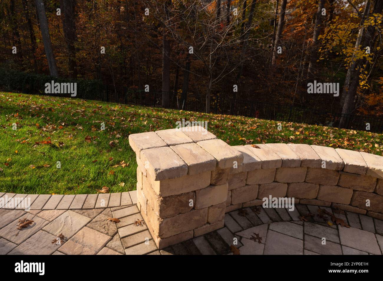 Primo piano di un patio in pietra ricurvo circondato da un cortile erboso ricoperto di foglie autunnali, che offre un'atmosfera calda e invitante all'aperto. Foto Stock