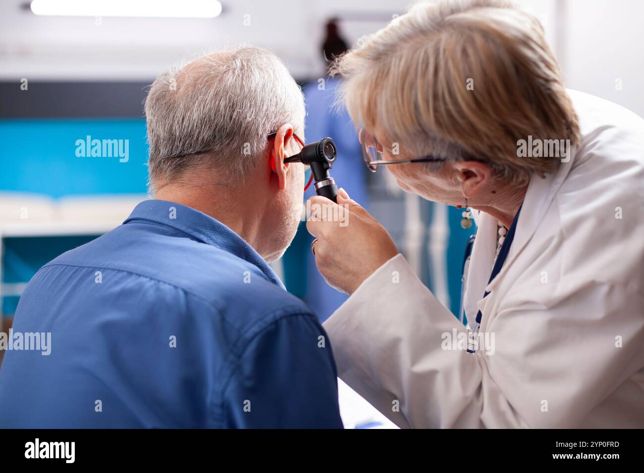 L'uomo in pensione seduto in sala d'ospedale subisce test uditivi come specialista di sesso femminile senior esegue esame medico con otoscopio. Medico anziano che controlla l'orecchio di un paziente pensionato maschio in clinica. Foto Stock