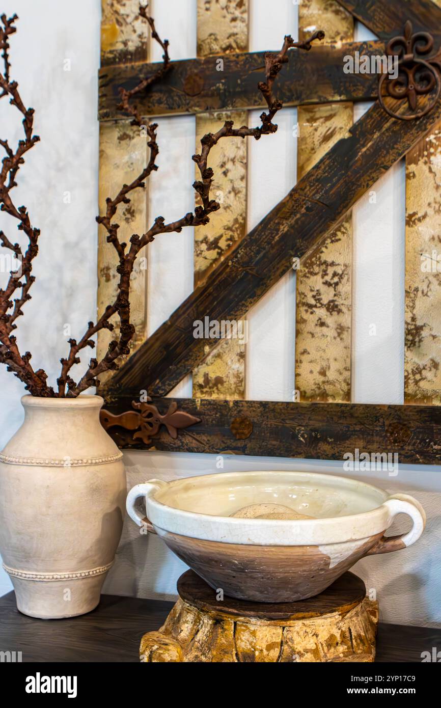 Un vaso in ceramica realizzato a mano regala delicati rami aridi all'avanguardia, mentre una ciotola in argilla rustica si appoggia delicatamente su un piedistallo in legno. Foto Stock