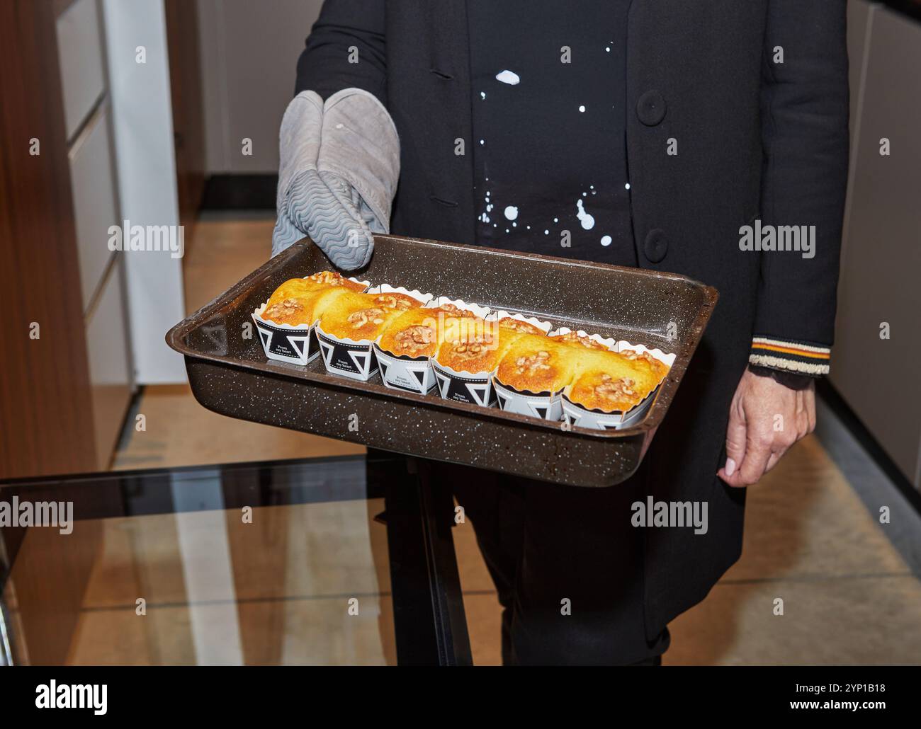 Un vassoio di muffin appena sfornati con crosta dorata, tenuto da una persona che indossa un guanto resistente al calore, in un ambiente di cucina. Foto Stock