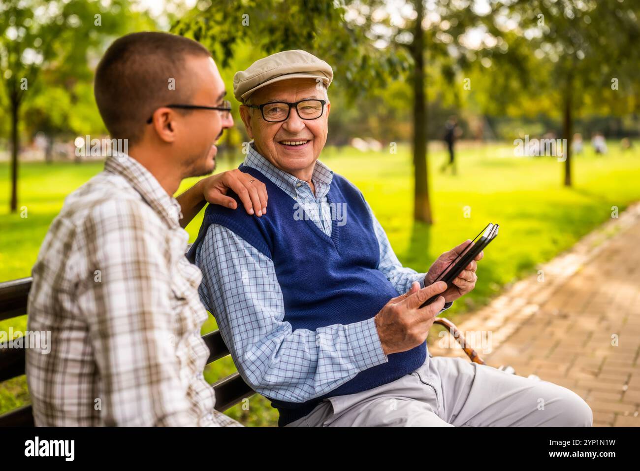 Ritratto di nonno felice e nipote nel parco. Stanno trascorrendo del tempo insieme e utilizzano un tablet digitale. Foto Stock