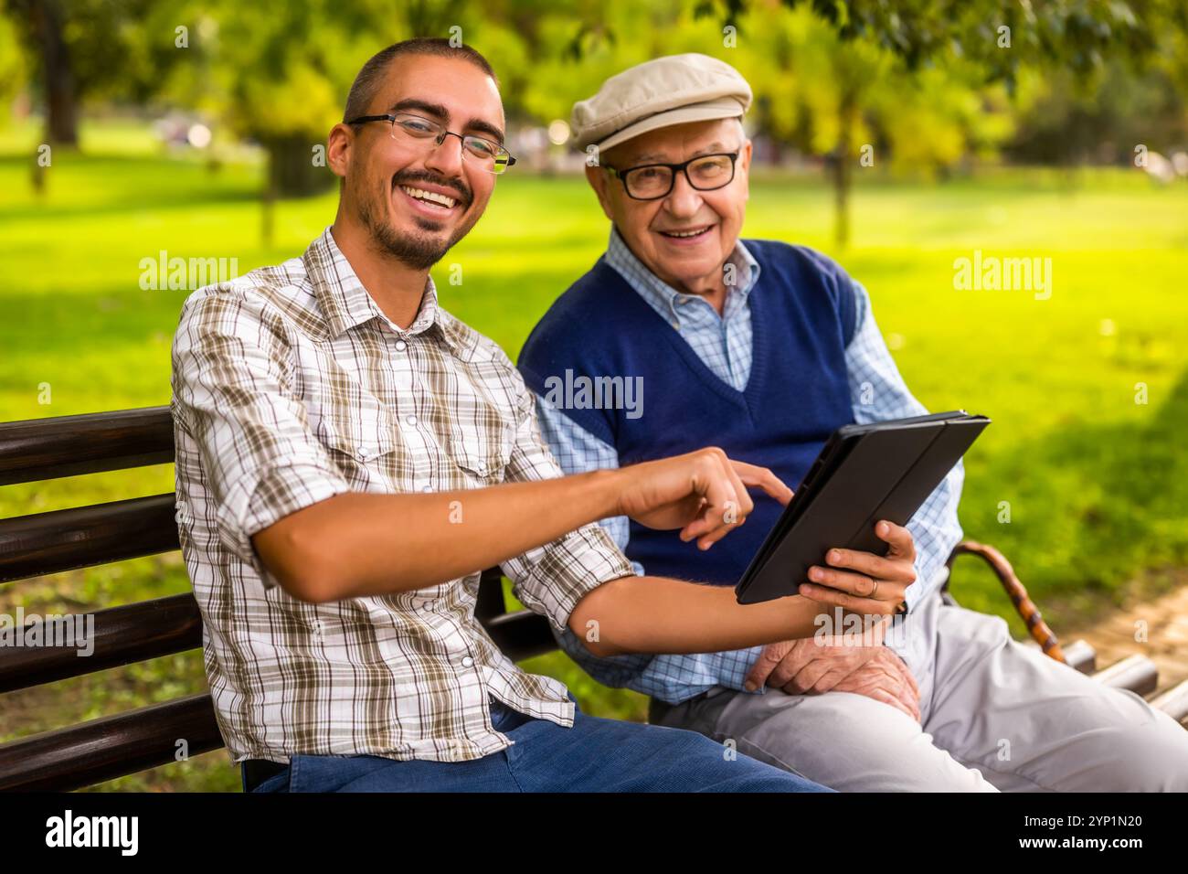 Ritratto di nonno felice e nipote nel parco. Stanno trascorrendo del tempo insieme e utilizzano un tablet digitale. Foto Stock