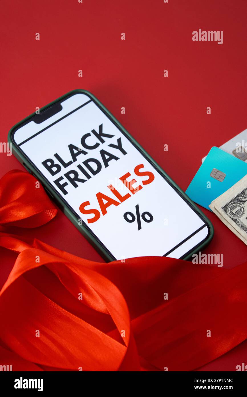 Vista dall'alto dello schermo di uno smartphone che mostra una vendita online del Black Friday su sfondo rosso con carte di credito e denaro Foto Stock