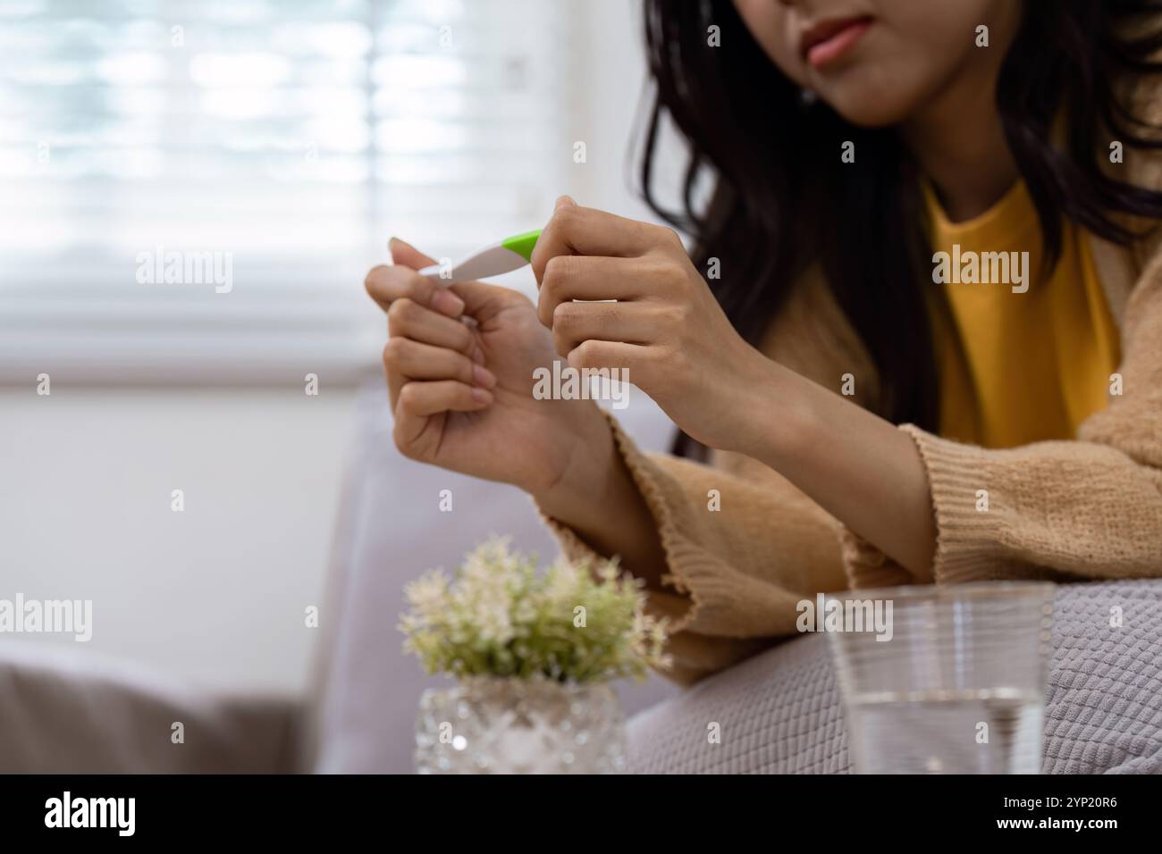 Donna che tiene il test di gravidanza seduta sul divano nel luminoso soggiorno con luce naturale e atmosfera accogliente Foto Stock