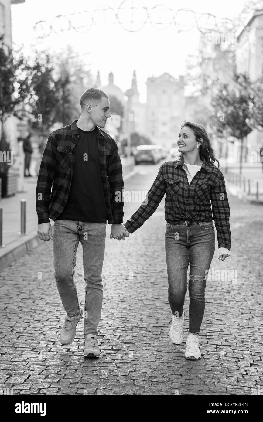 Un affascinante momento bianco e nero di una coppia che cammina mano nella mano su una strada acciottolata. Foto Stock