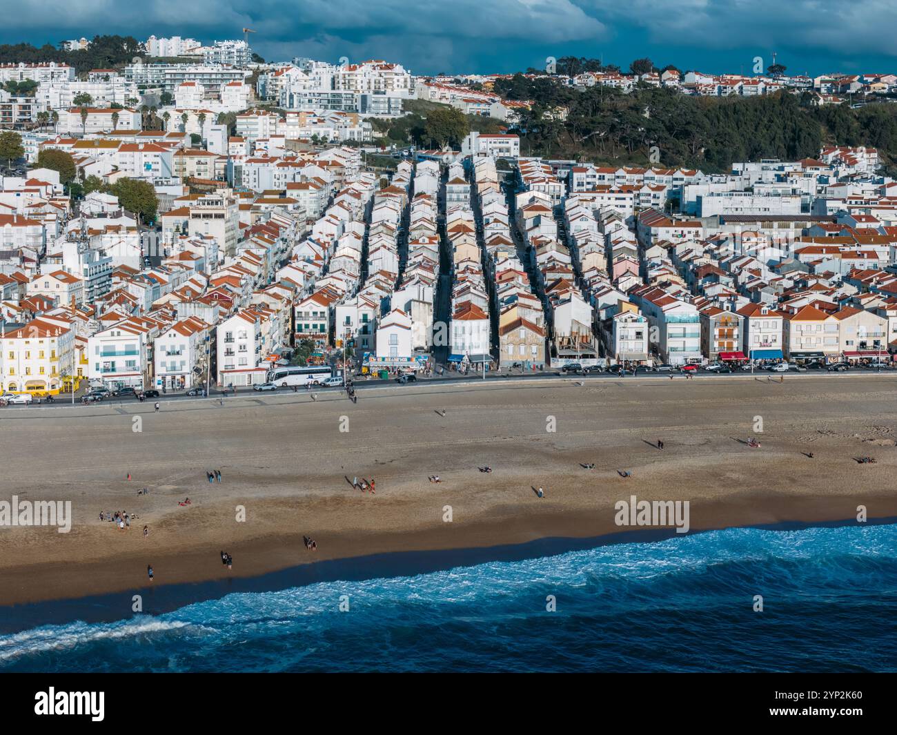 La vivace spiaggia, che rivela file di affascinanti case con tetti rossi e persone che si godono la spiaggia sabbiosa sotto un cielo limpido, Nazare, Oeste Foto Stock