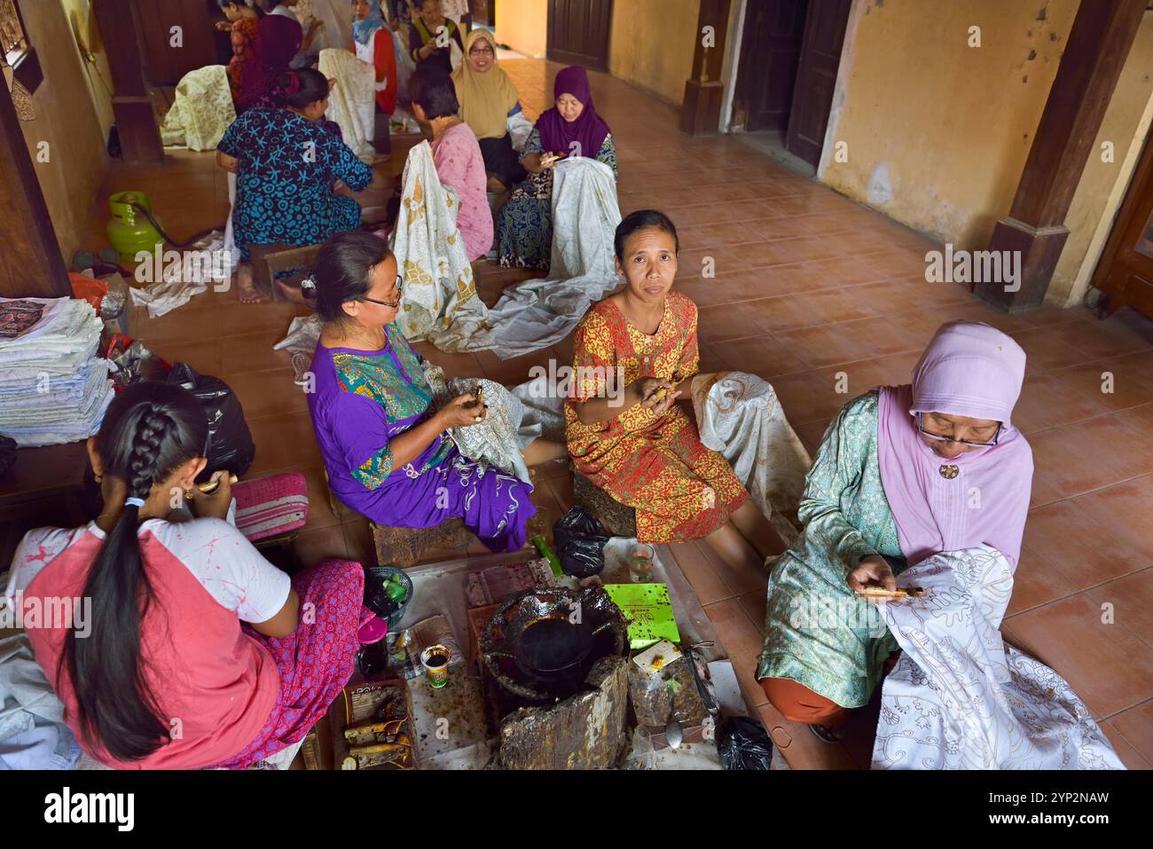 Donne che utilizzano uno strumento simile a una penna (cantando) per applicare cera calda liquida nel processo di fabbricazione del batik, laboratorio di batik di Wirakuto, Pekalongan, isola di Giava, Indonesia Foto Stock