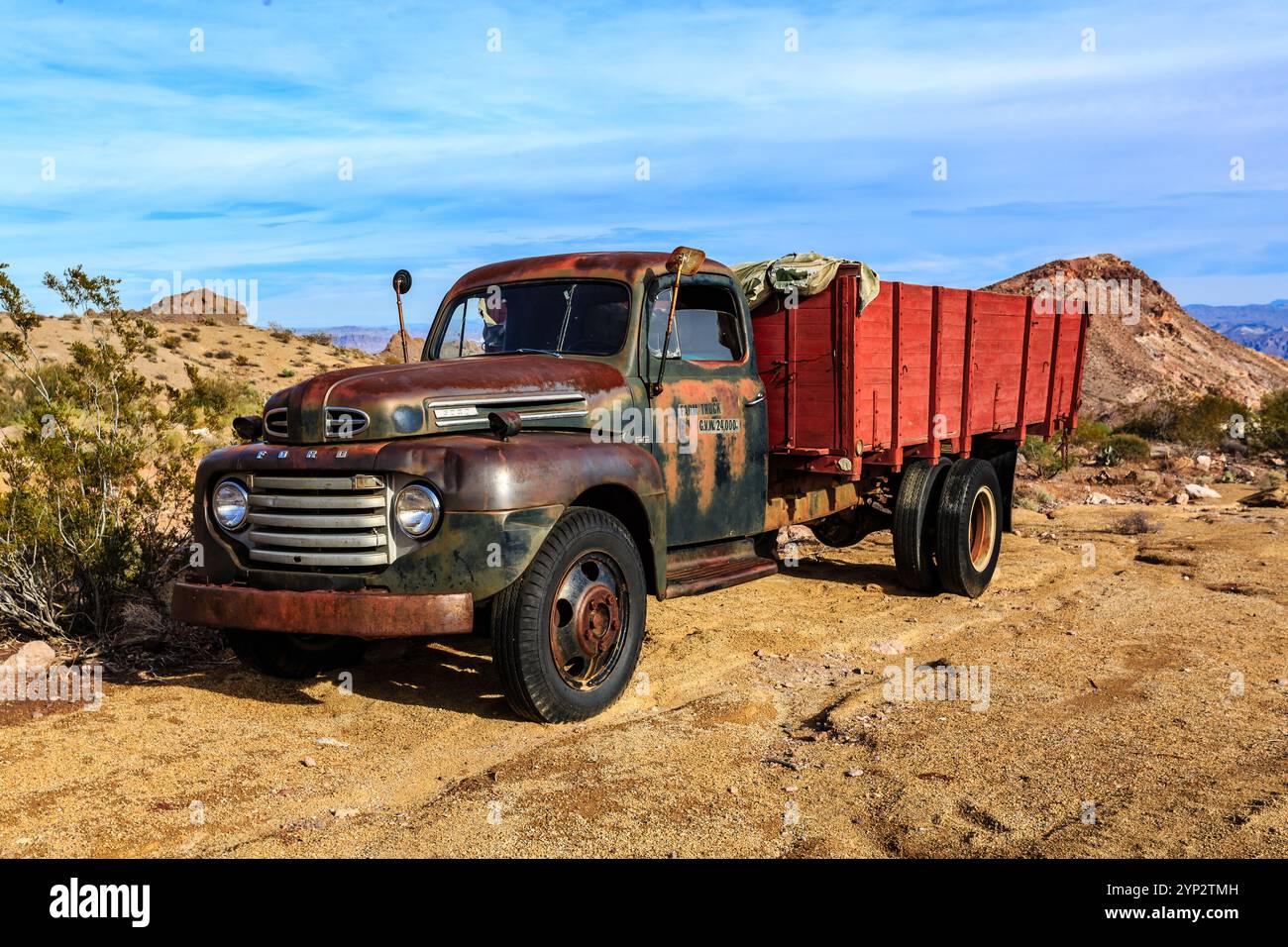 Un vecchio camion Ford è parcheggiato su una strada sterrata. Il carrello è arrugginito e presenta un lavoro di verniciatura rosso sbiadito. La scena è desolata e silenziosa, senza altri veicoli Foto Stock