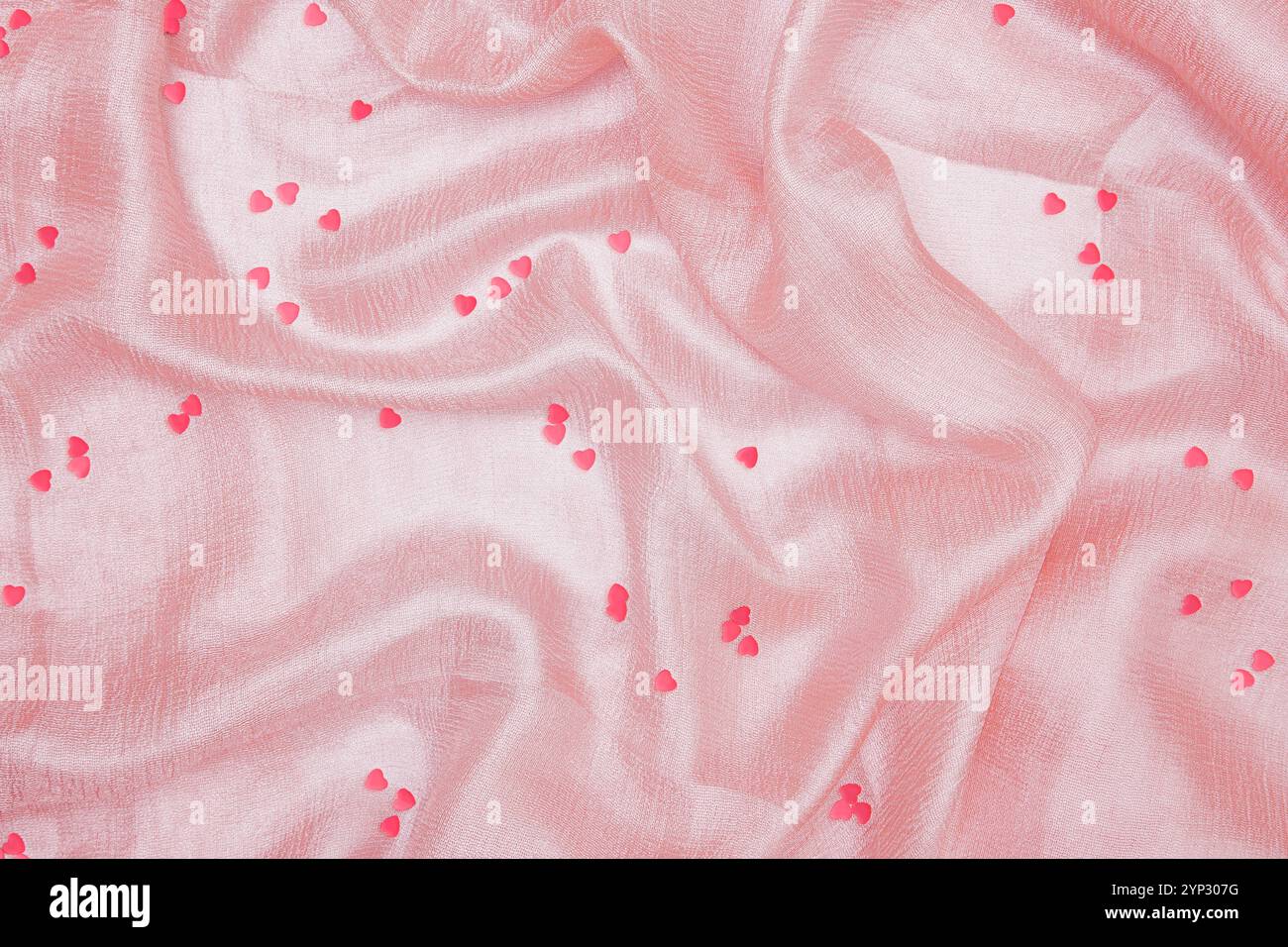 Piccoli cuori rosa adagiati su un tessuto di seta rosa chiaro Foto Stock