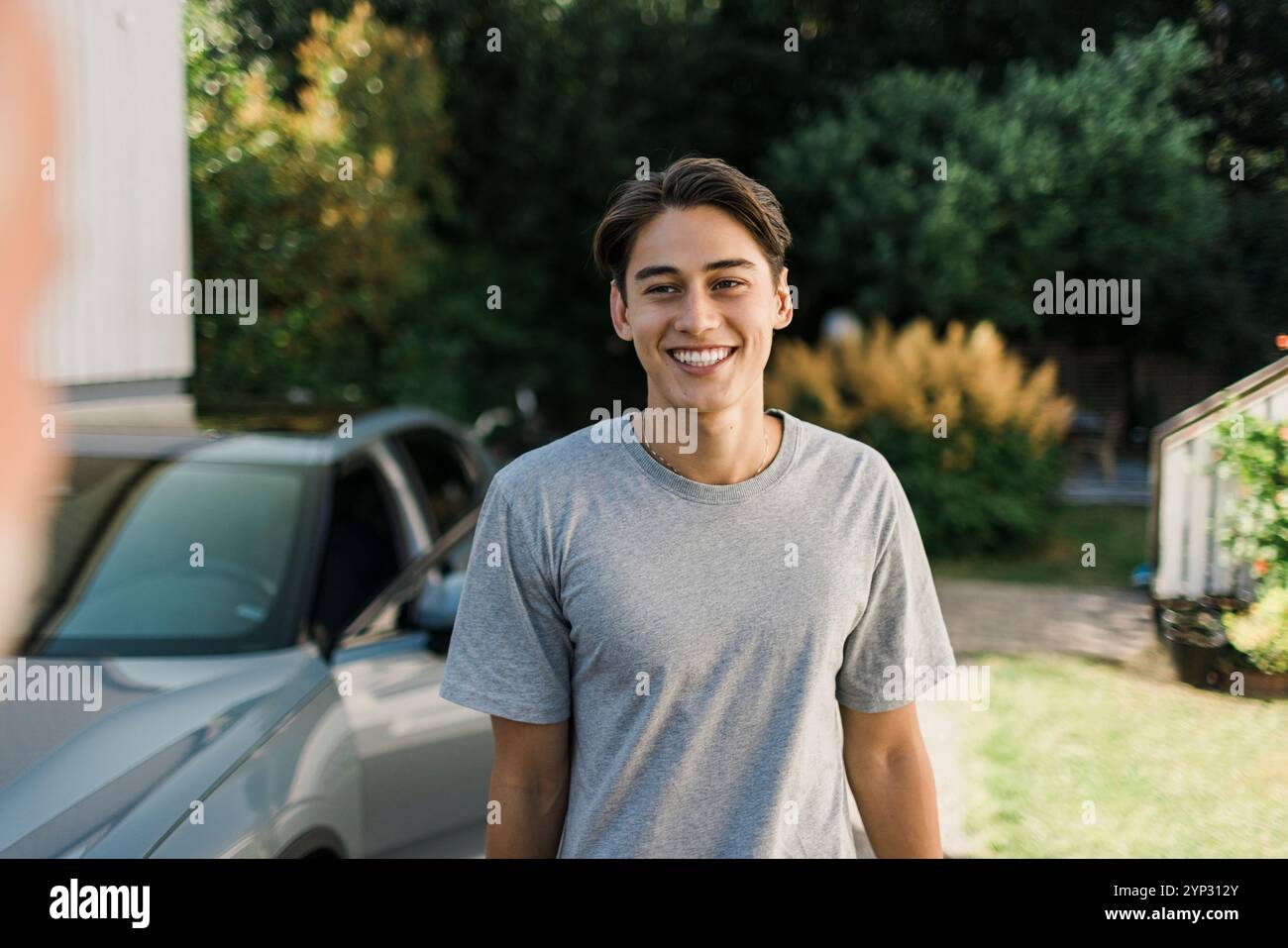 Giovane felice che indossa una t-shirt grigia in piedi nel cortile posteriore Foto Stock