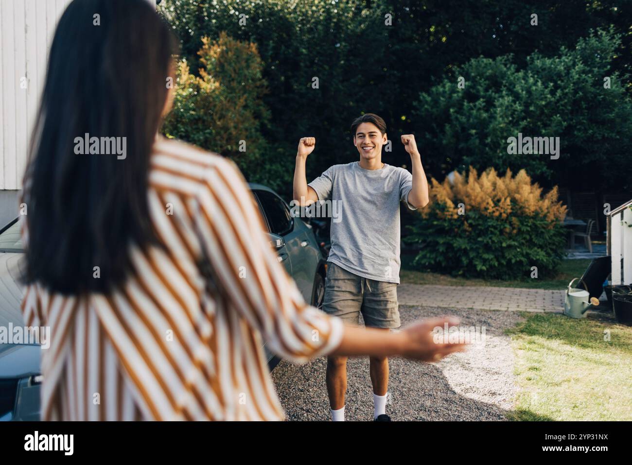 Giovane allegro che tiene il pugno mentre festeggia con la madre nel cortile posteriore Foto Stock