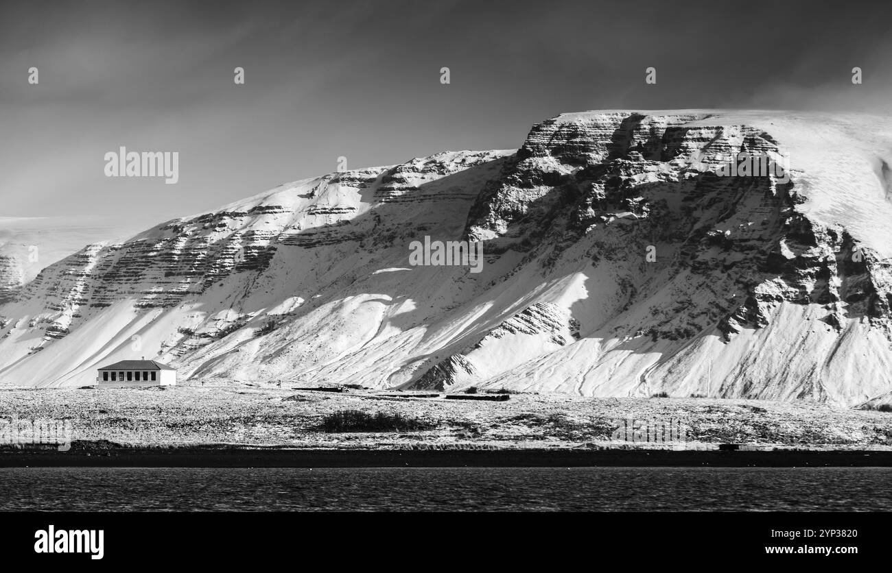 Paesaggio con montagne costiere innevate sotto il cielo scuro e drammatico. Area di Reykjavik, Islanda. Fotografia panoramica in bianco e nero Foto Stock