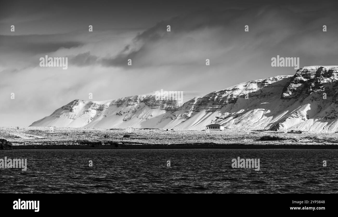 Paesaggio islandese con montagne costiere innevate sotto il cielo scuro e drammatico. Area di Reykjavik, Islanda. Fotografia panoramica in bianco e nero Foto Stock