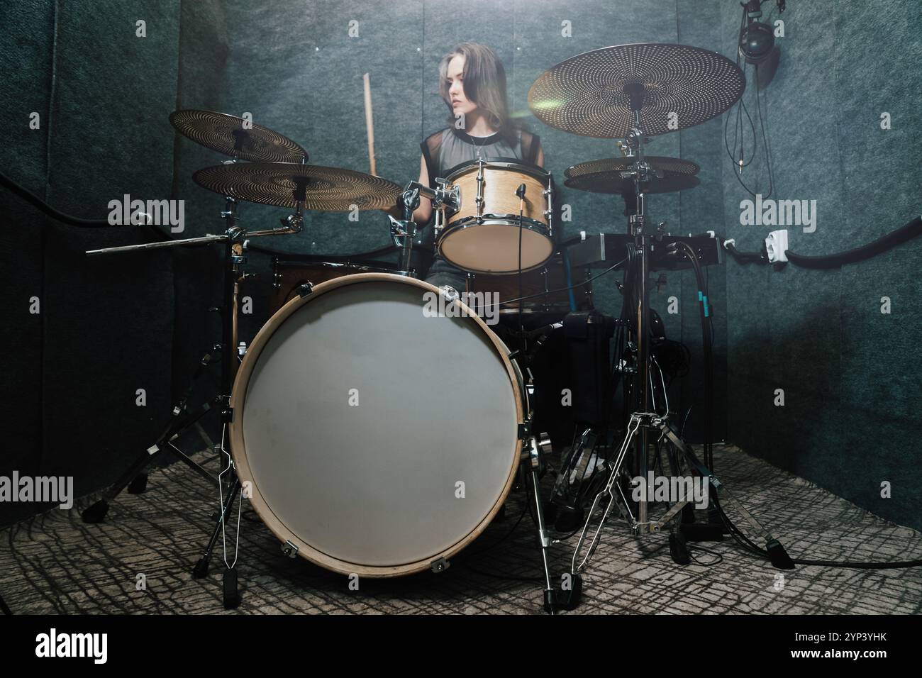 Batterista femminile che si esibisce su un set di batteria professionale in studio insonorizzato, concentrandosi sul ritmo e sull'energia della creazione di musica dal vivo. La scena mette in risalto la passione per la musica, le prestazioni e l'espressione artistica. Foto Stock