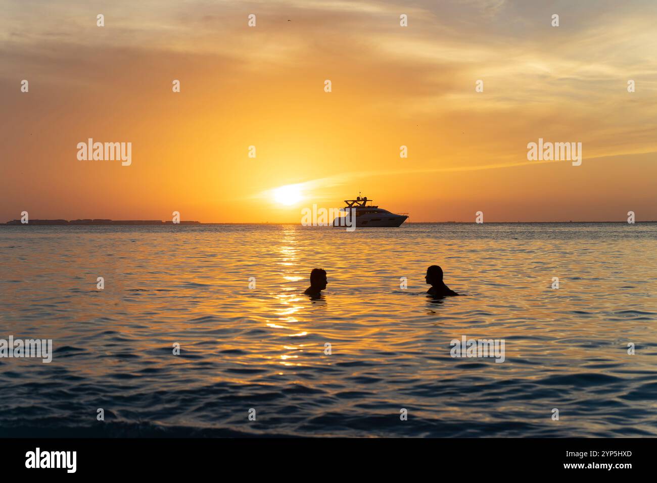 Due amanti in vacanza guardano un tramonto sul Mar dei Caraibi su un'isola tropicale con spiaggia deserta e barca all'orizzonte in Messico Foto Stock