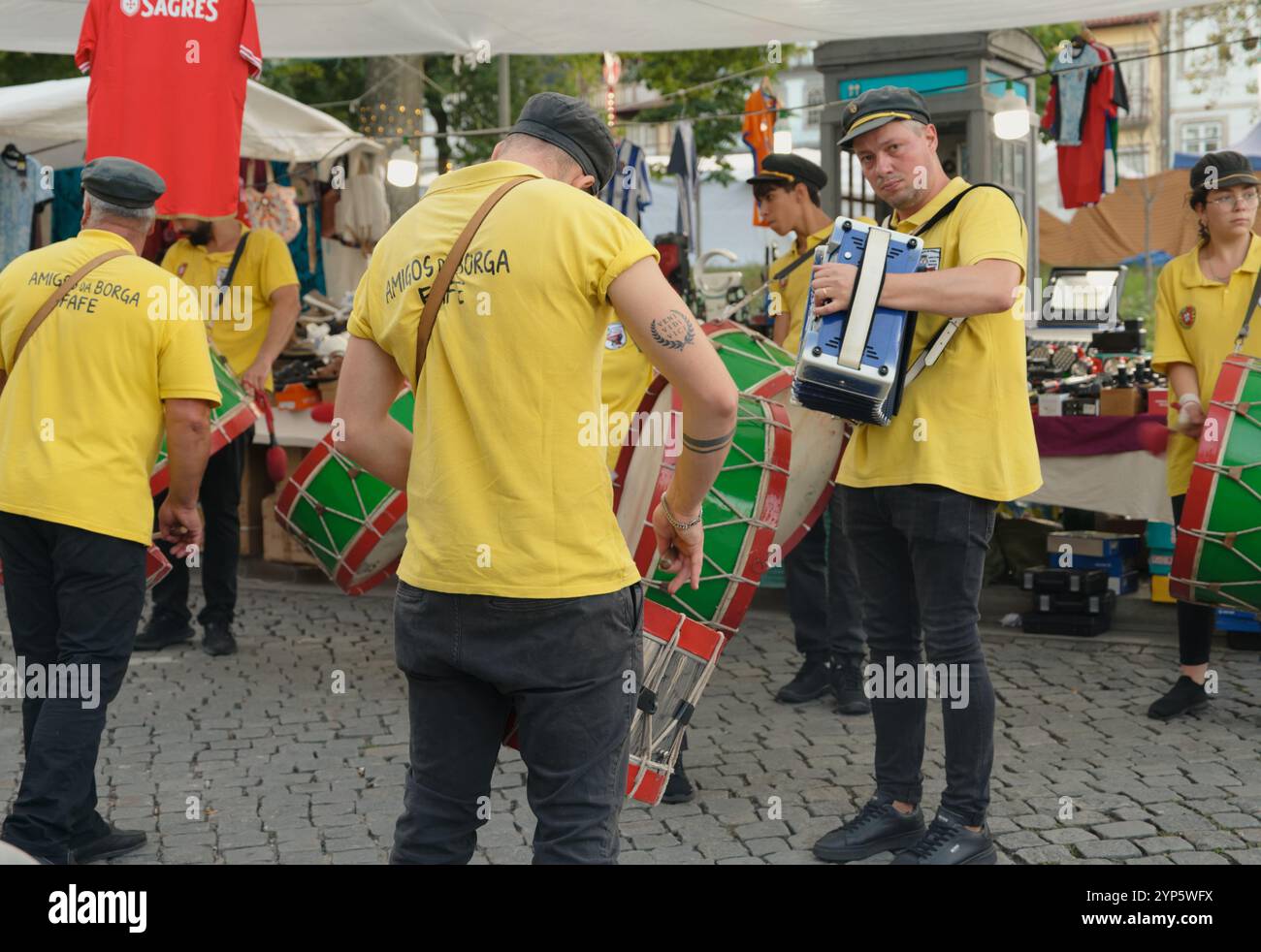 Batteristi e fisarmonicisti in giallo vibrante si esibiscono nelle vivaci vie del mercato di Guimarães durante i festival della città Foto Stock