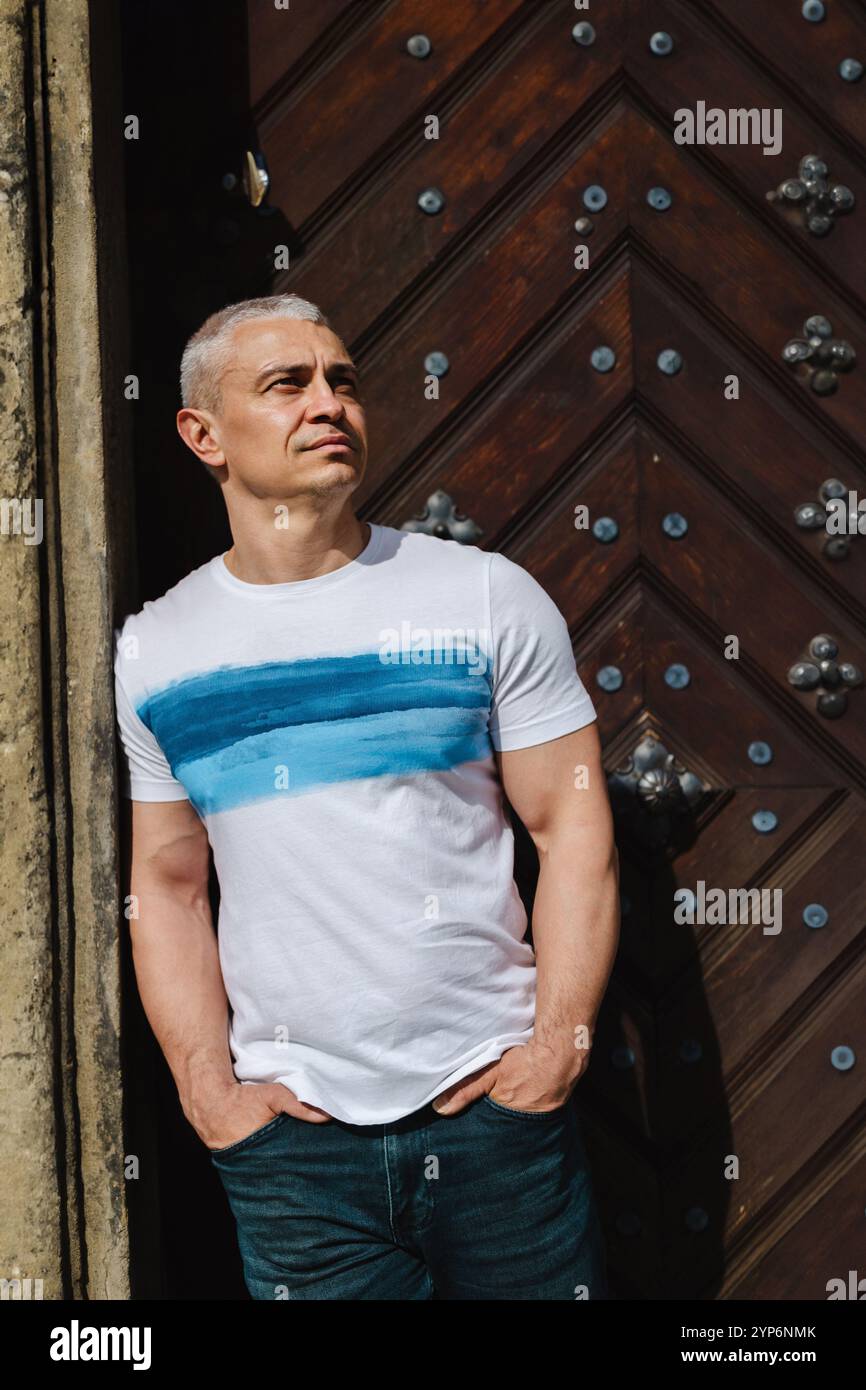 Un uomo con una camicia bianca a strisce blu si erge davanti a una porta di legno Foto Stock