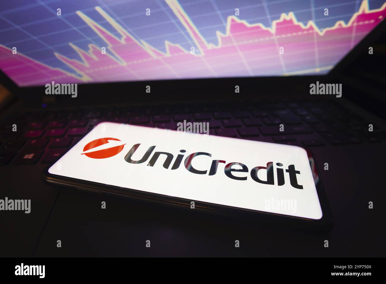 In questa immagine viene mostrato l'UniCredit visualizzato su uno schermo di uno smartphone, con una rappresentazione grafica del mercato azionario sullo sfondo Foto Stock