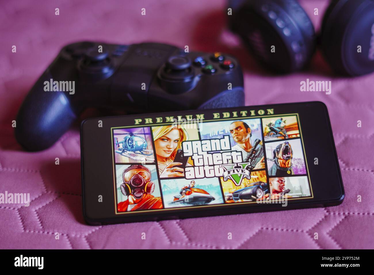 In questa immagine, il logo Grand Theft Auto V (GTA) viene visualizzato sullo schermo di uno smartphone, accanto a un gamepad Foto Stock