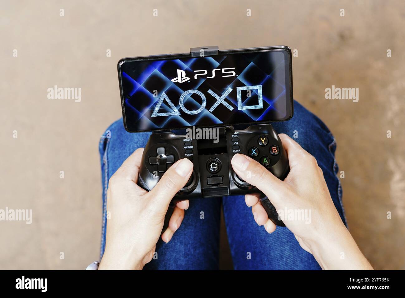 In questa immagine, una persona che gioca su un joystick e il logo PlayStation Showcase sono visualizzati sullo schermo di uno smartphone Foto Stock