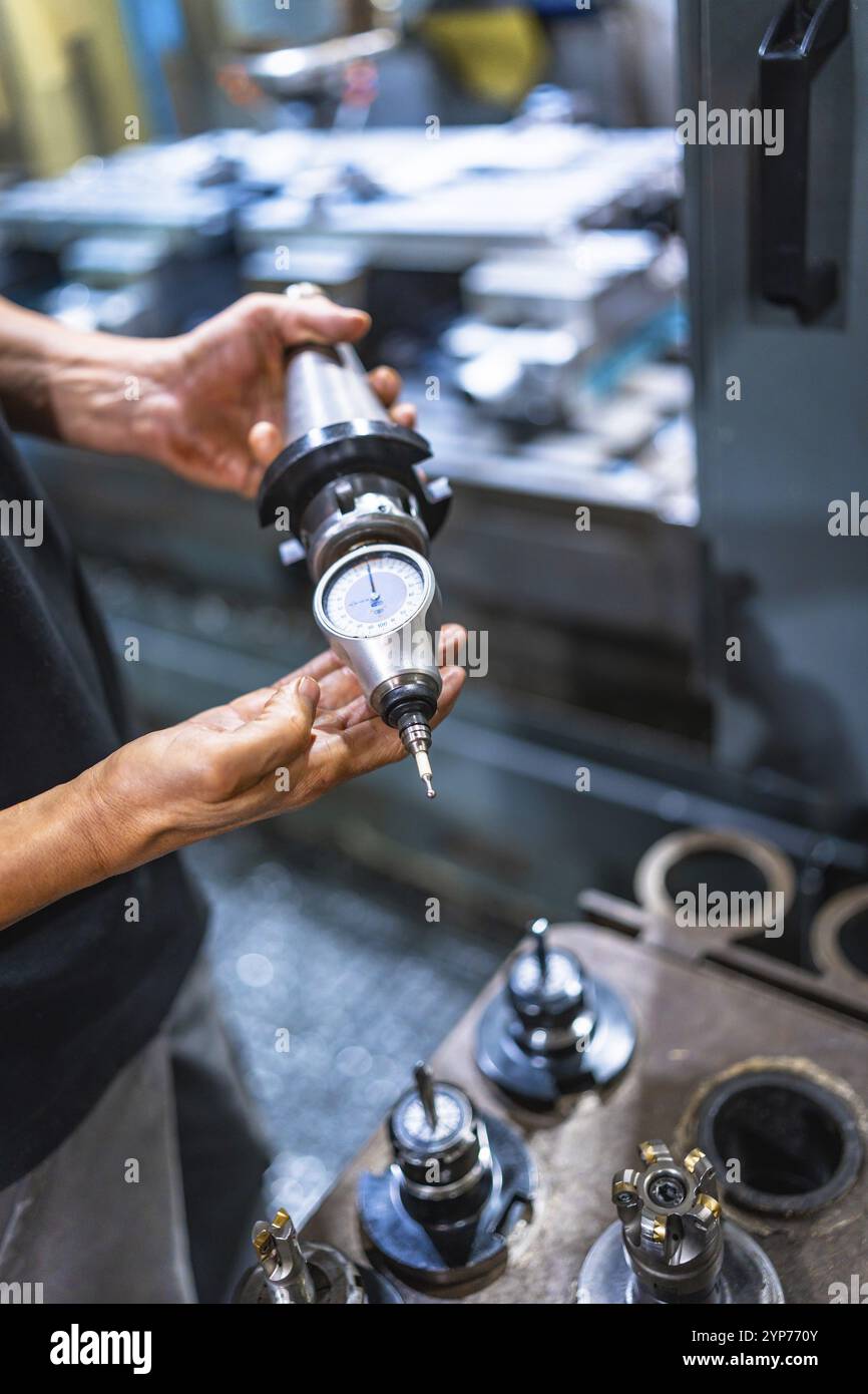 Primo piano verticale di un tecnico caucasico maschile irriconoscibile che tiene in mano un pezzo di fresatrice che lavora in fabbrica Foto Stock