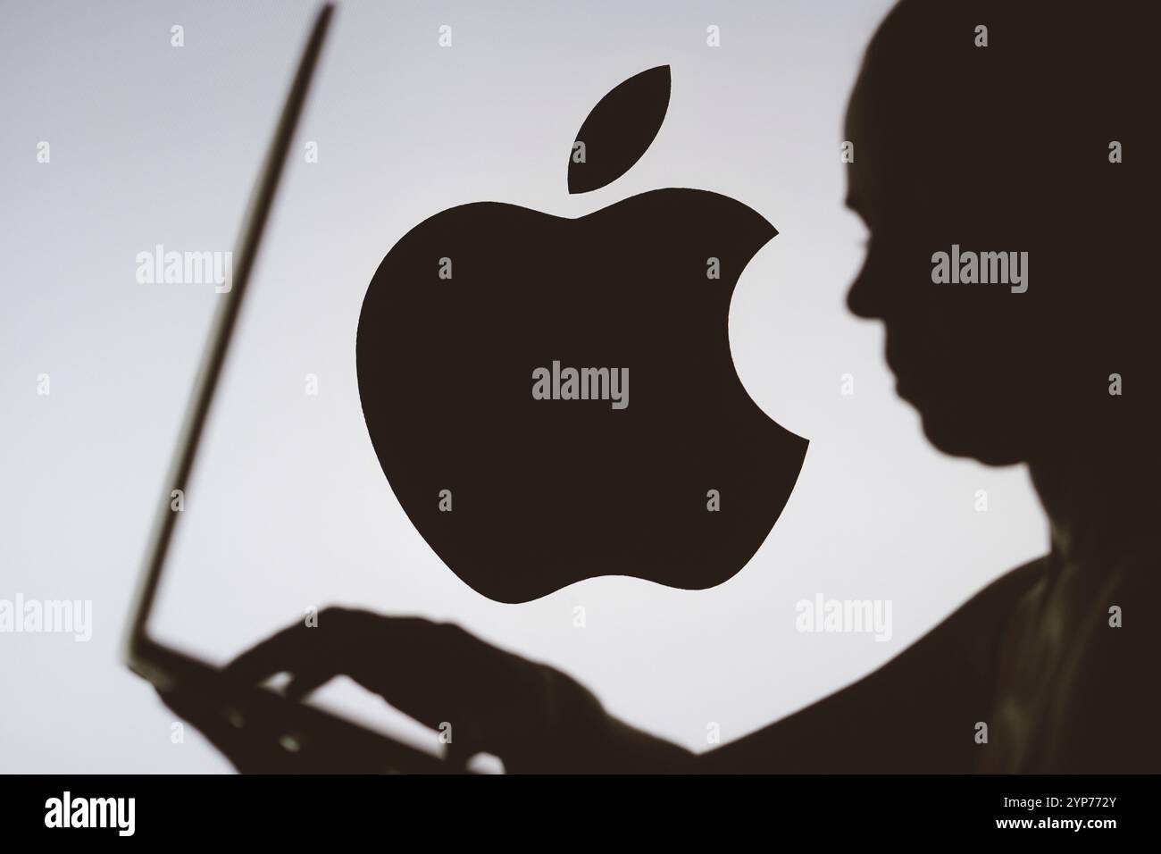In questa illustrazione fotografica, il logo Apple viene visualizzato sullo sfondo di una silhouette di una persona che utilizza un notebook Foto Stock