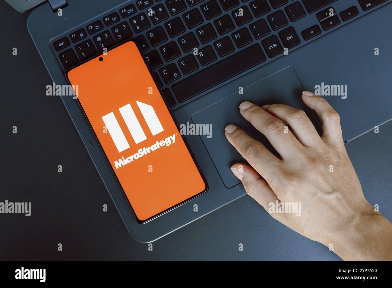 In questa immagine, il logo MicroStrategy Incorporated viene visualizzato sullo schermo di uno smartphone accanto a una persona che utilizza un computer portatile Foto Stock