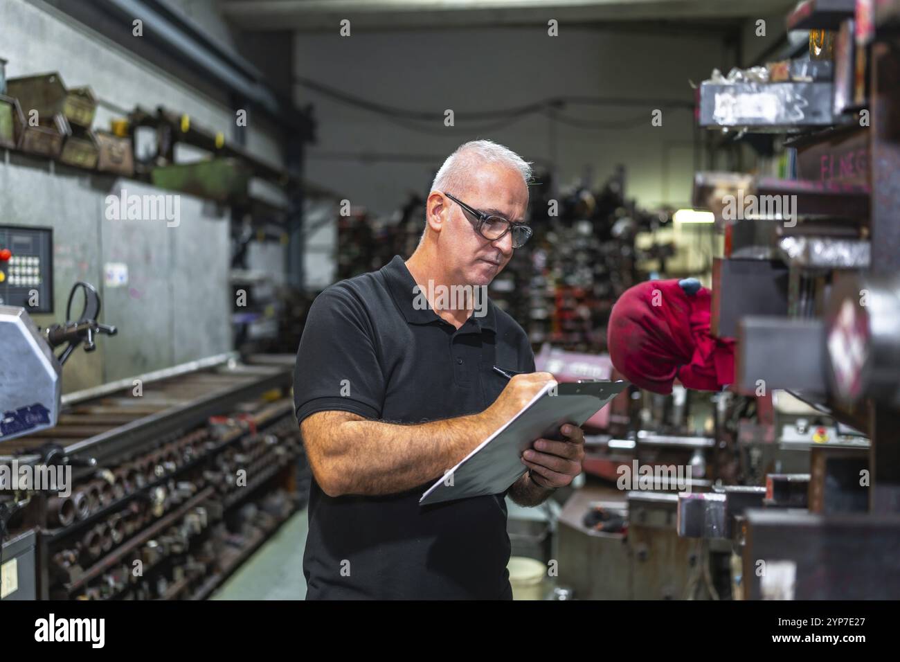 Lavoratore maschio maturo concentrato che tiene gli appunti e scrive mentre fa l'inventario in una fabbrica metallurgica Foto Stock