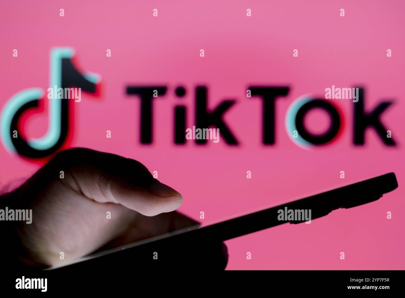 In questa illustrazione fotografica, il logo TikTok visto sullo sfondo di una persona che tiene in mano uno smartphone Foto Stock