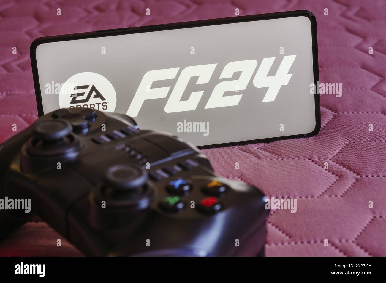 In questa immagine, il logo EA SPORTS FC 24 viene visualizzato sullo schermo di uno smartphone, accanto a un gamepad Foto Stock