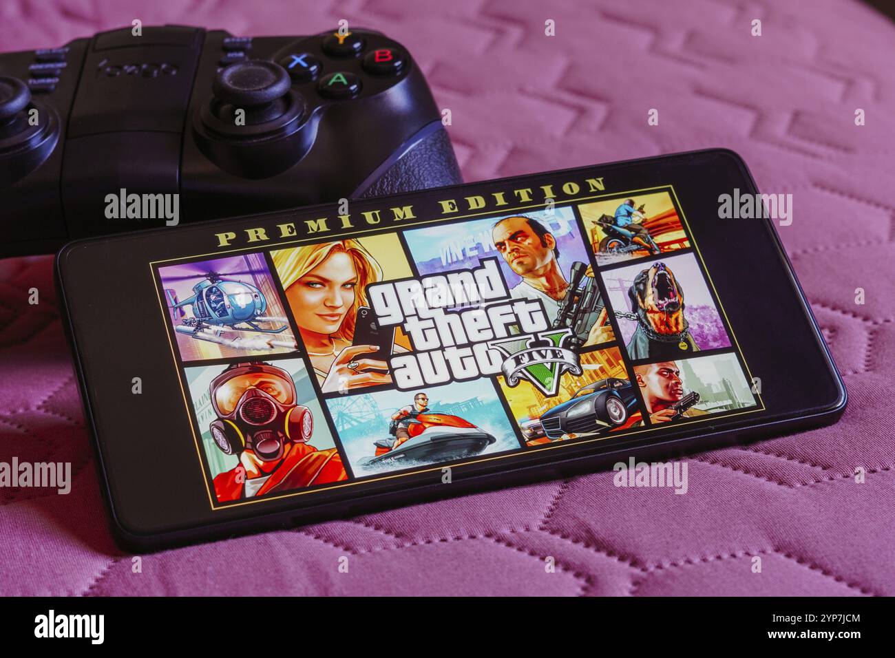 In questa immagine, il logo Grand Theft Auto V (GTA) viene visualizzato sullo schermo di uno smartphone, accanto a un gamepad Foto Stock