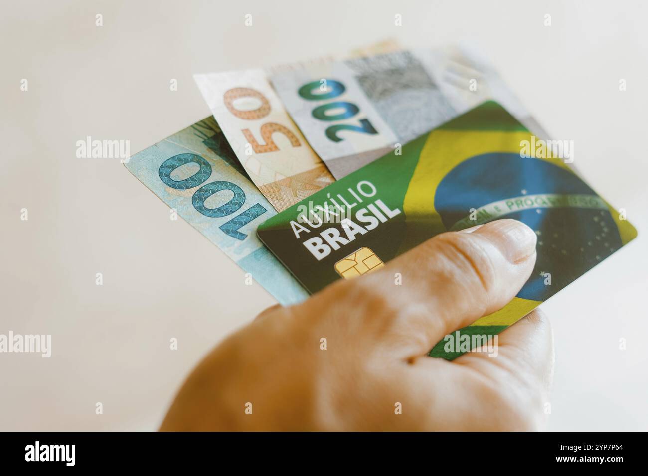 In questa illustrazione fotografica una donna che tiene in mano la carta Auxilio Brasil (Bolsa Familia) con banconote in denaro reale provenienti dal Brasile Foto Stock