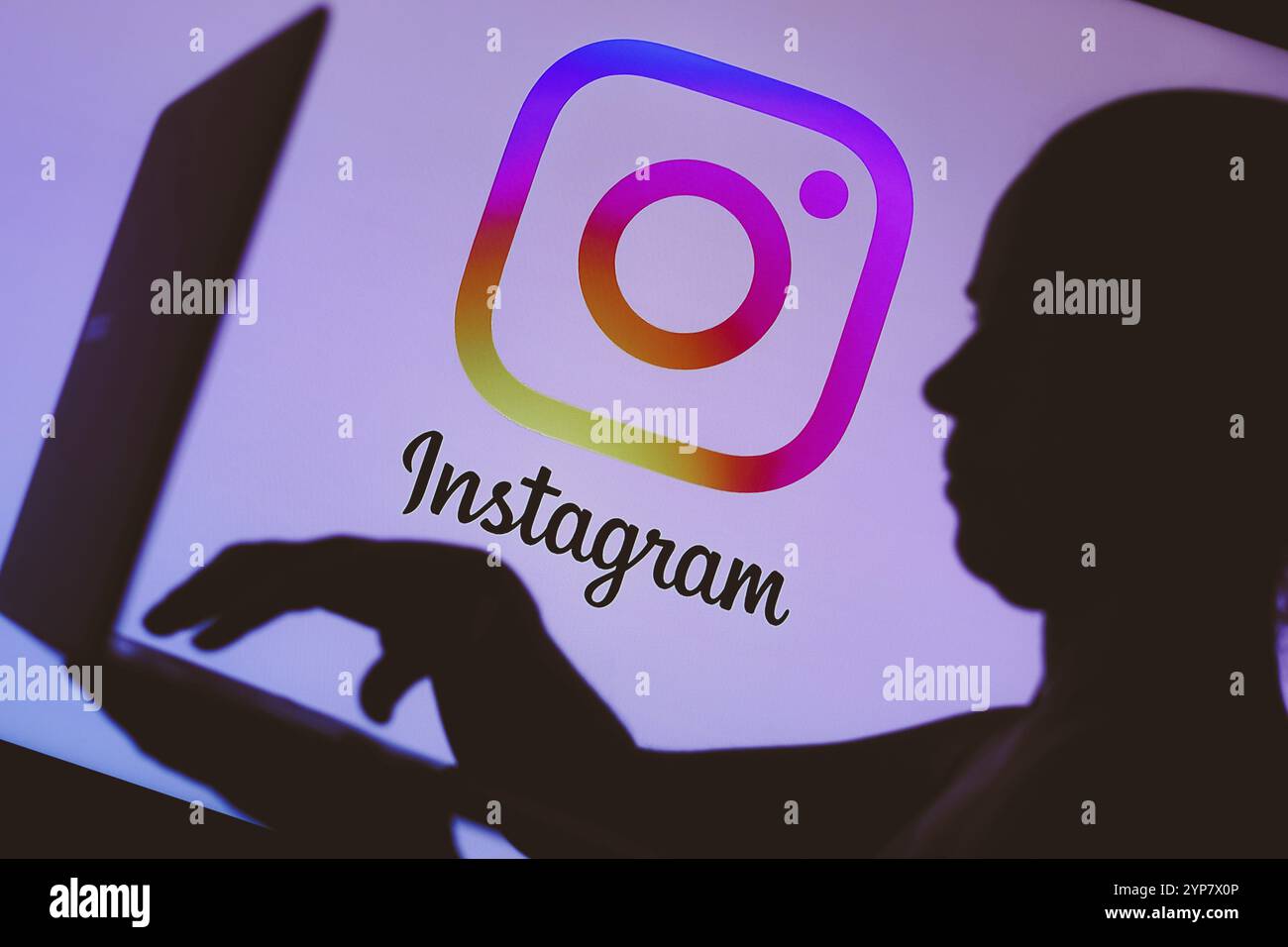In questa illustrazione fotografica, il logo Instagram è visibile sullo sfondo di una silhouette di una persona che utilizza un notebook Foto Stock