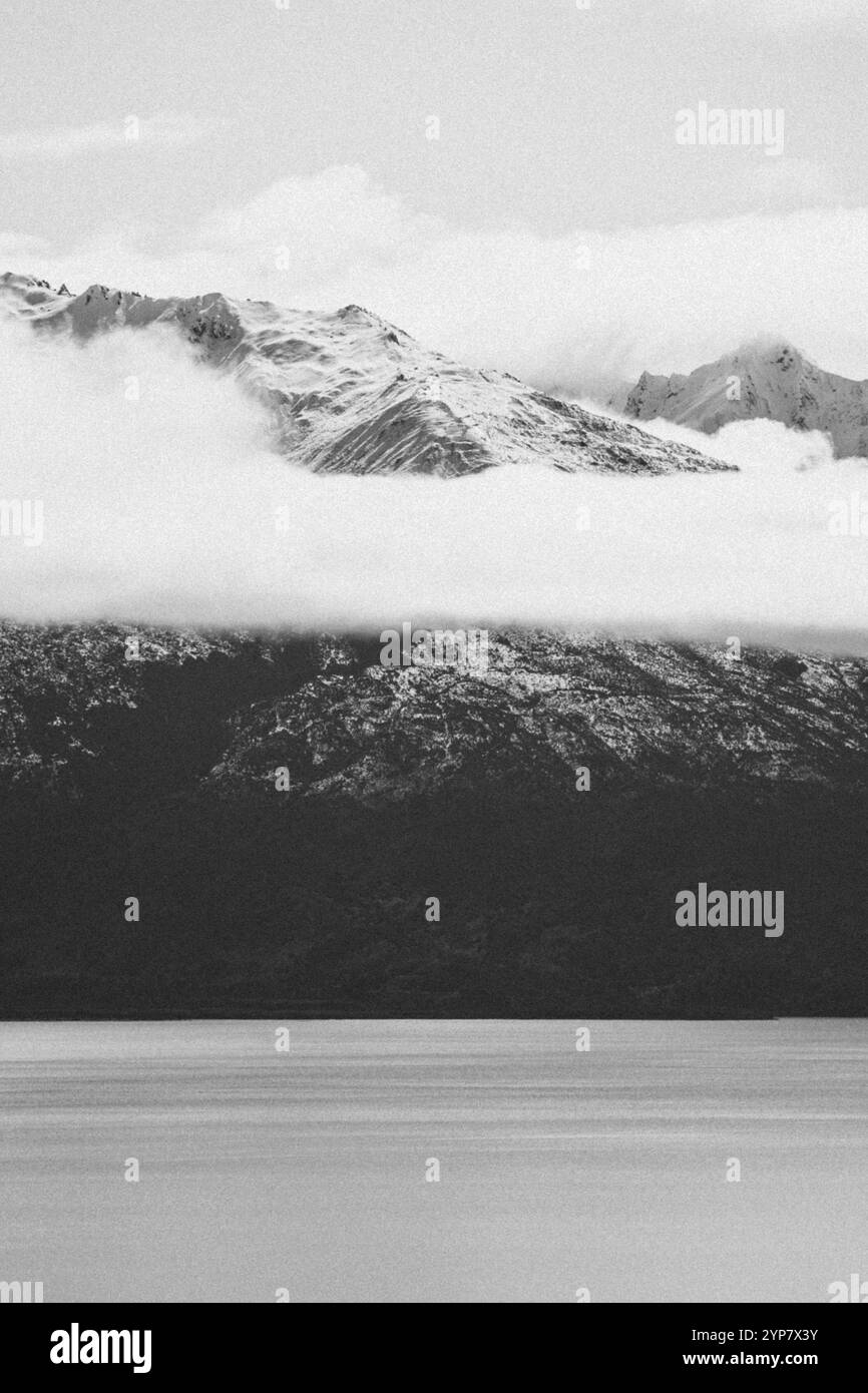 Montagne innevate sorgono dalle nuvole sopra un lago calmo in una fotografia in bianco e nero, Wanaka, nuova Zelanda, Oceania Foto Stock