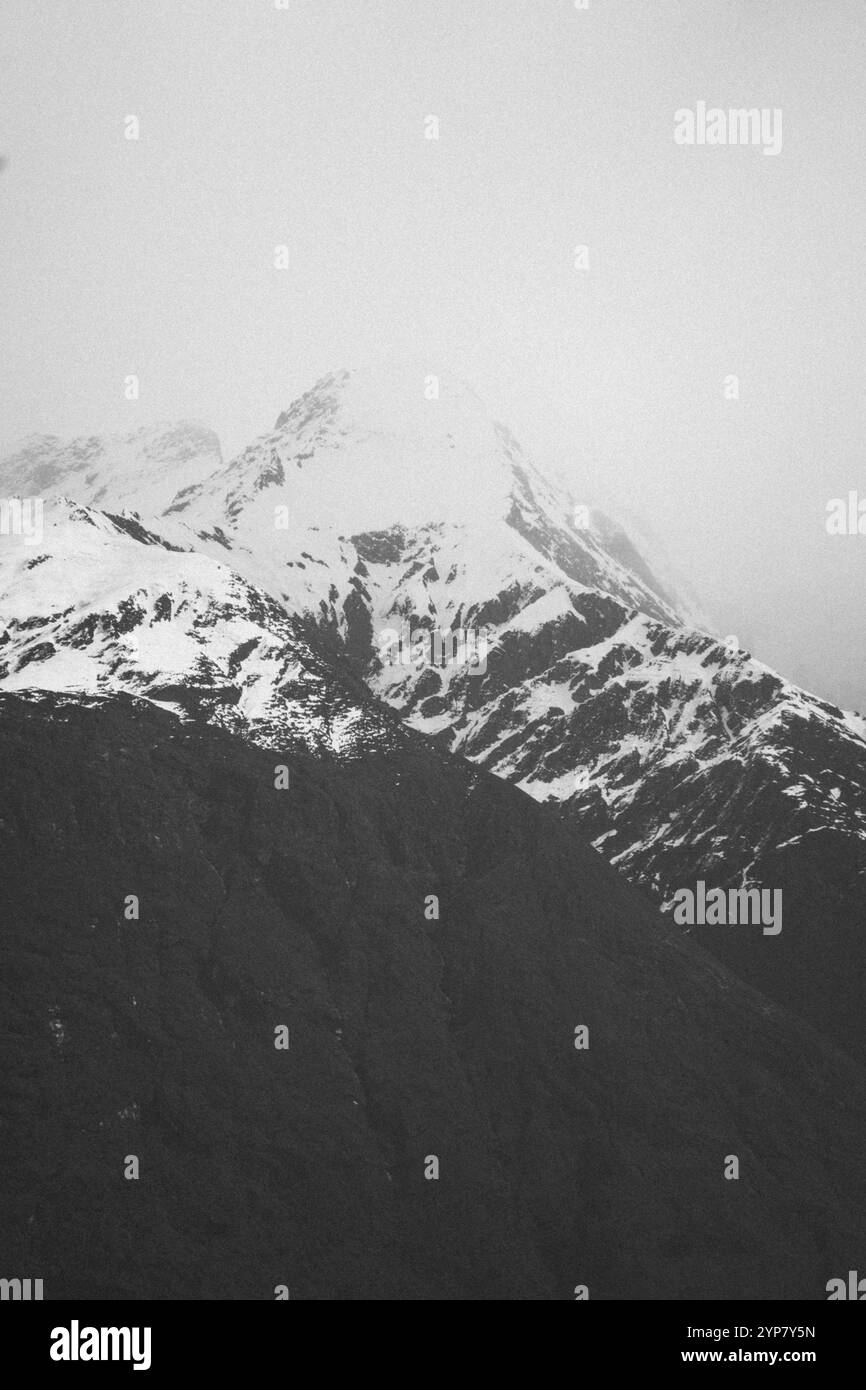 Immagine monocromatica di vette innevate avvolte dalla nebbia, Cattle Flat, Wanaka, nuova Zelanda, Oceania Foto Stock