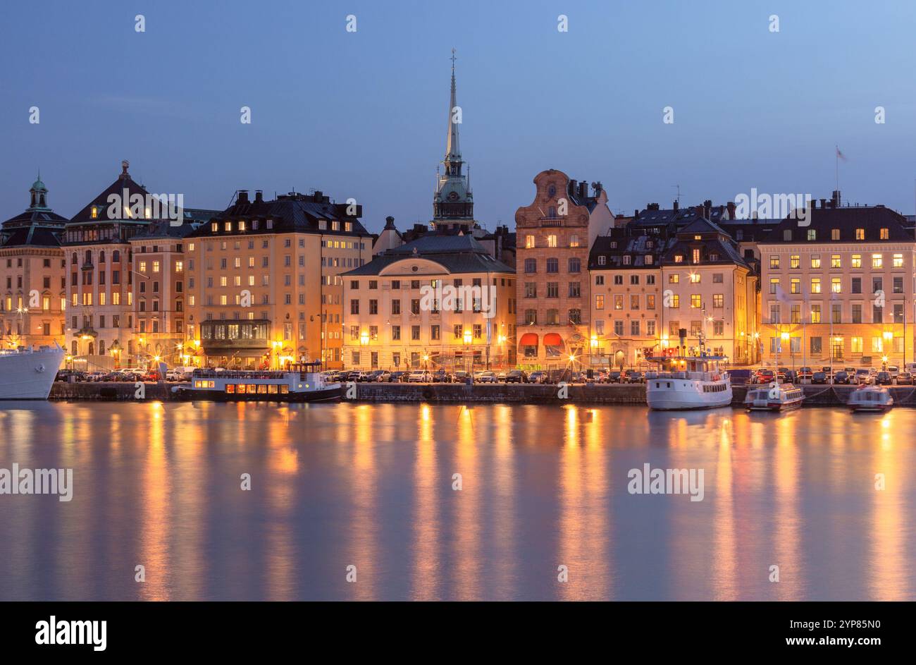 Vista panoramica sul lungomare di Stoccolma al tramonto che mostra gli edifici storici illuminati e la guglia della chiesa Storkyrkan di Stoccolma, Svezia Foto Stock