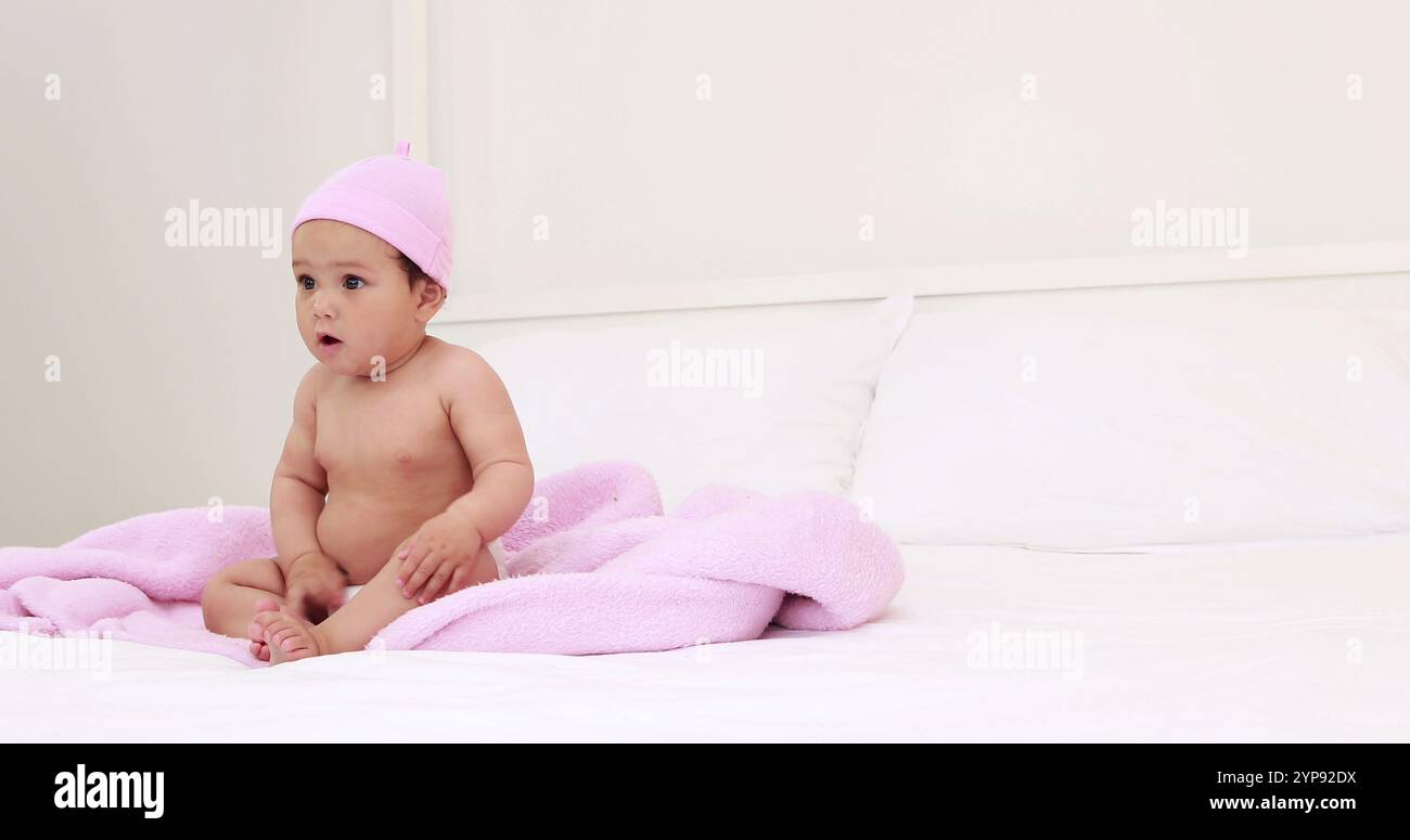 Bambino carino con cappuccio rosa seduto a casa Foto Stock