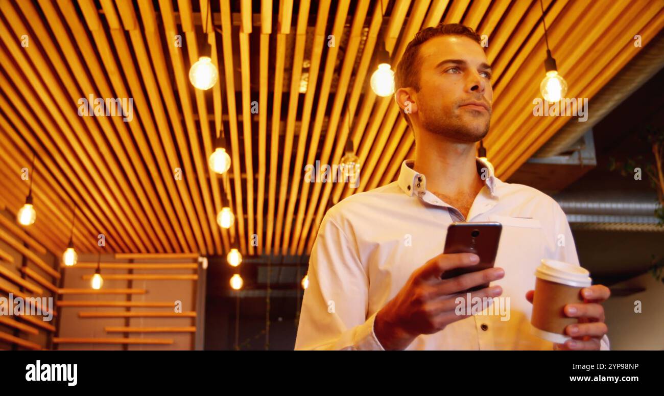 Vista ad angolo basso di un giovane e attraente dirigente maschile che usa il telefono cellulare mentre beve un caffè in una caffetteria Foto Stock