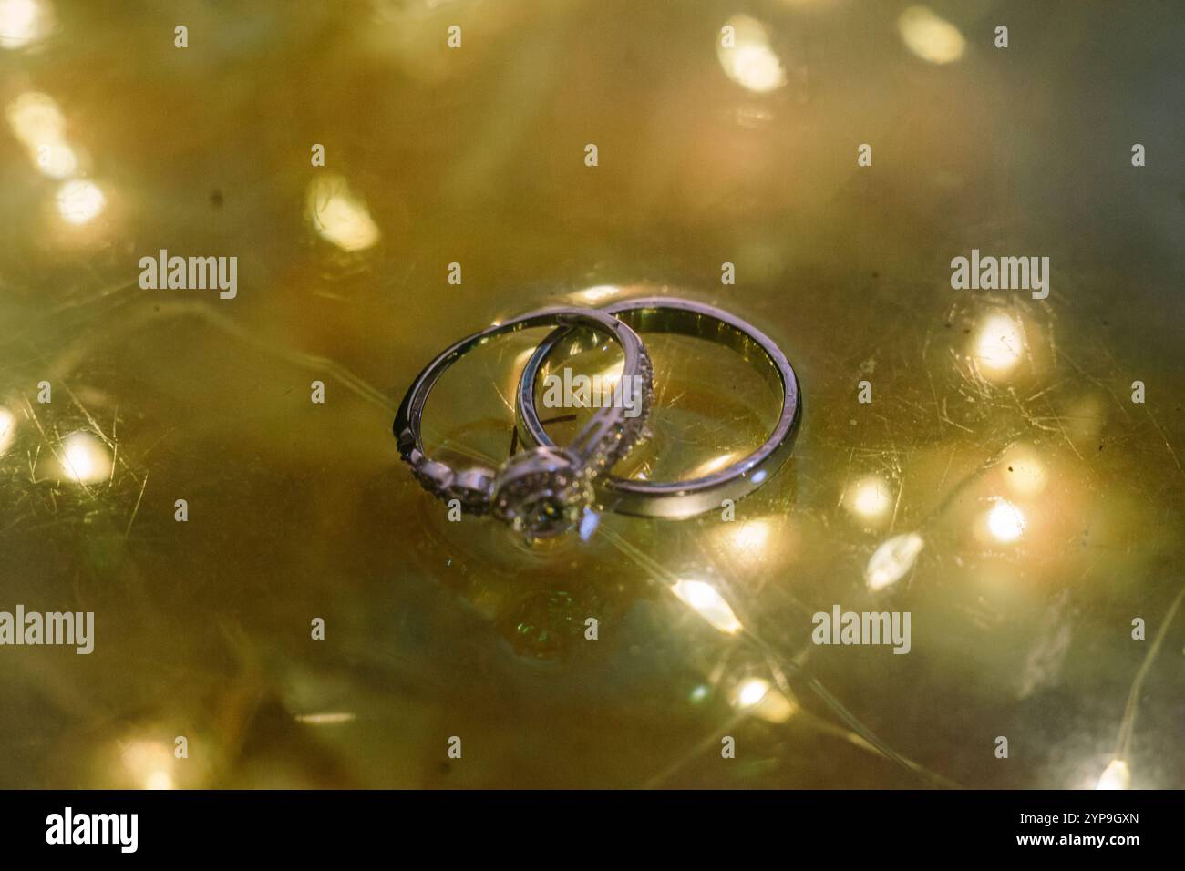 Le fedi nuziali sono esposte elegantemente su una lampada di vetro, riflettendo una luce soffusa, simboleggiando l'amore e l'impegno. Foto Stock