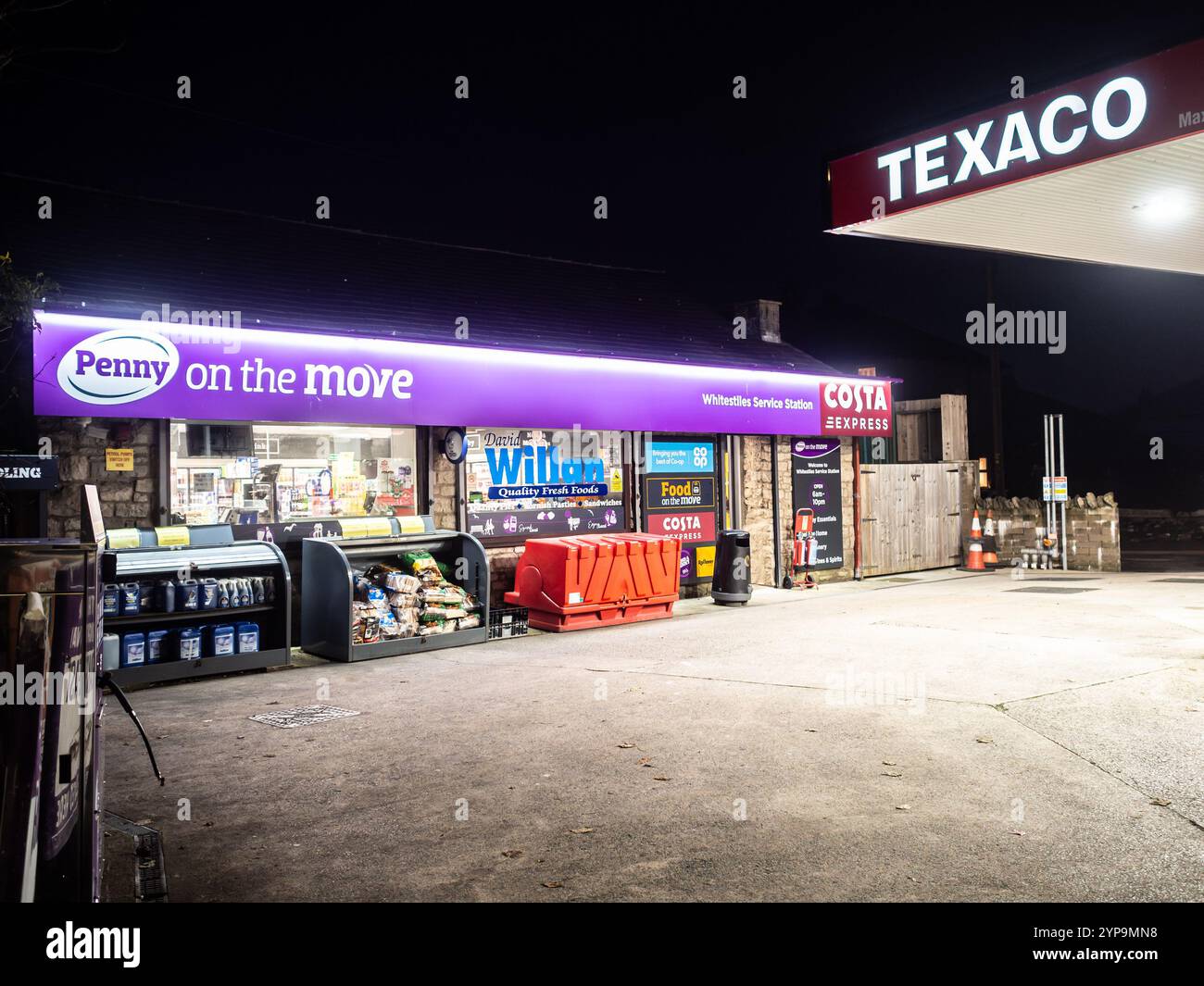 Stazione di servizio e negozio di alimentari Texaco Penny Petroleum a Kendal, Regno Unito, che brilla di luce in una sera d'inverno buia con un cartello Costa Express visibile. Foto Stock