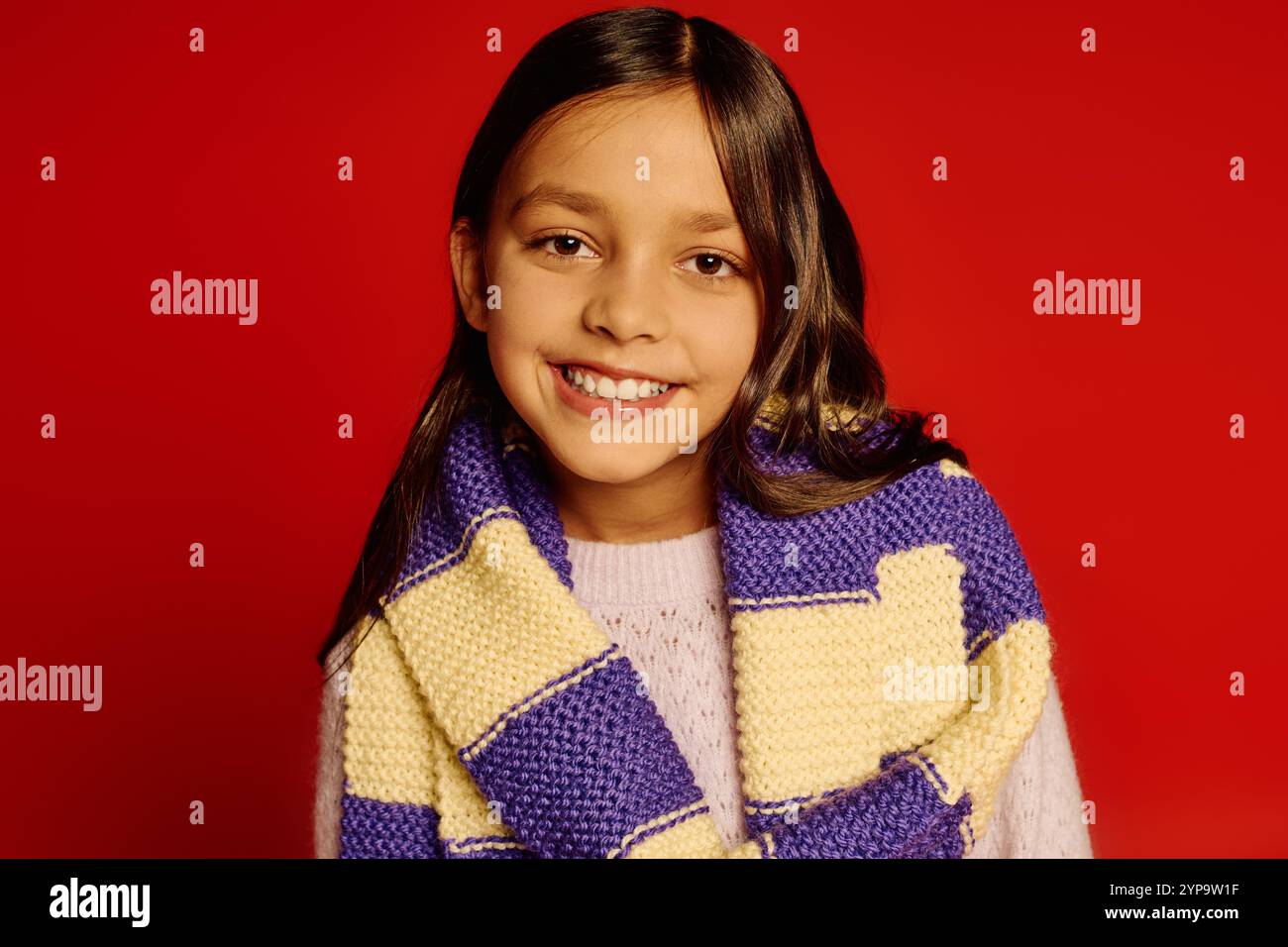 Ragazza sorridente che indossa una sciarpa accogliente, che irradia gioia e allegria festosa in un'atmosfera vivace. Foto Stock