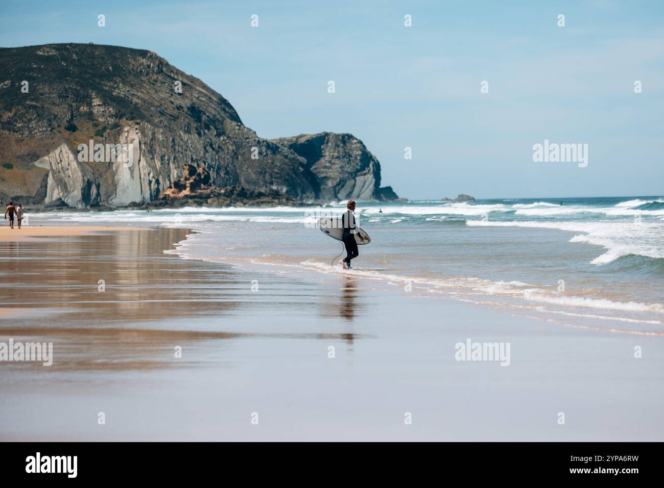 Surfista camminando verso le onde con le scogliere nelle vicinanze in portogallo Foto Stock