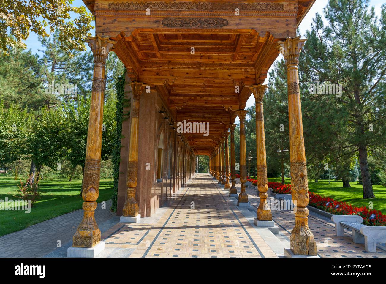 Un lungo corridoio con colonne di legno e una disposizione floreale rossa Foto Stock