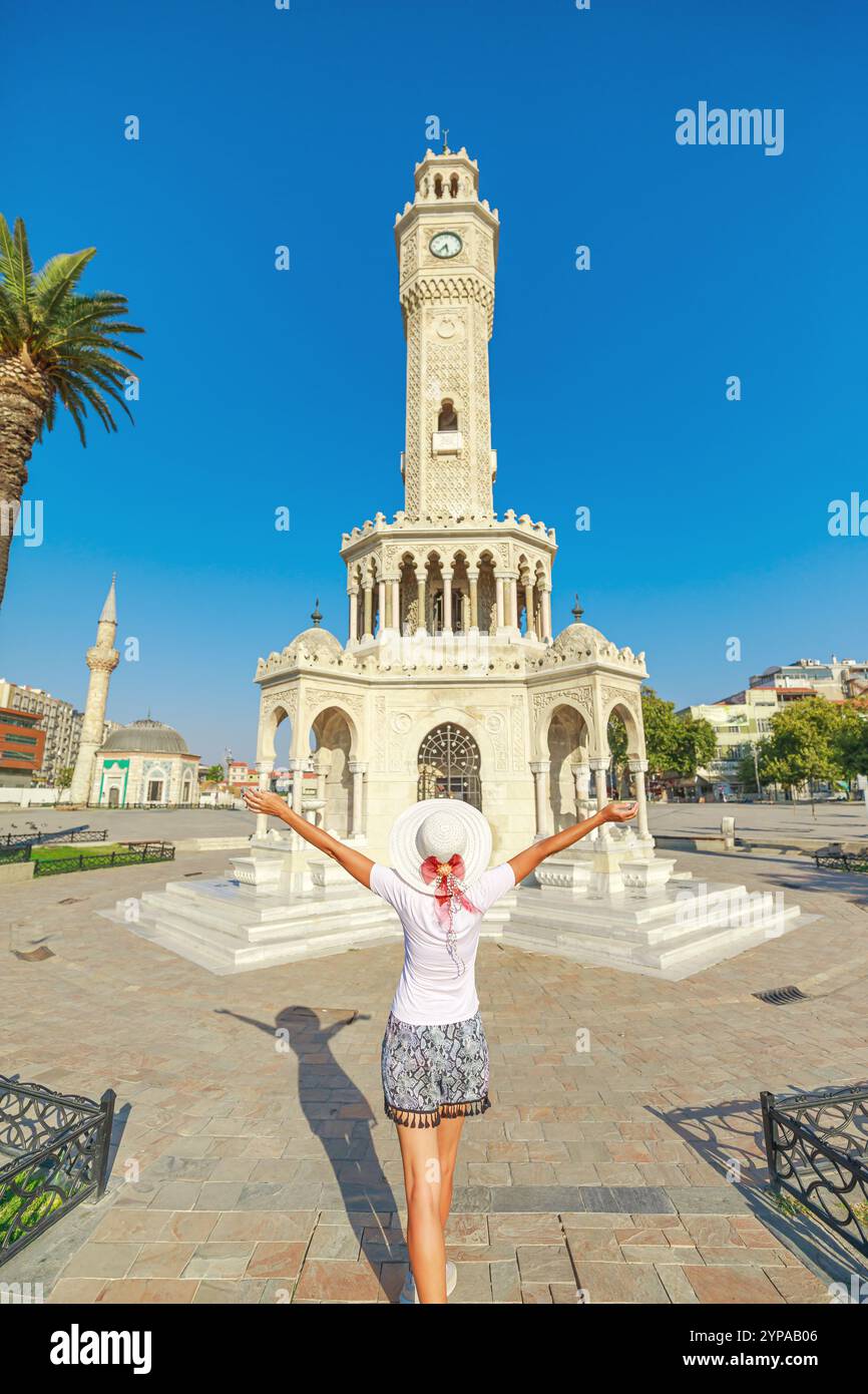 La donna turistica si erge stupita davanti alla Torre dell'Orologio in Piazza Konak a Smirne, una sentinella storica del tempo dal 1901. Circondato dalla vivace vita di Foto Stock